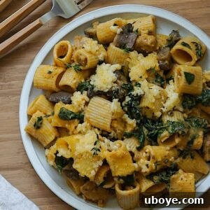 A dish of pumpkin pasta with kale and mushrooms served on a white plate, ready to be eaten.