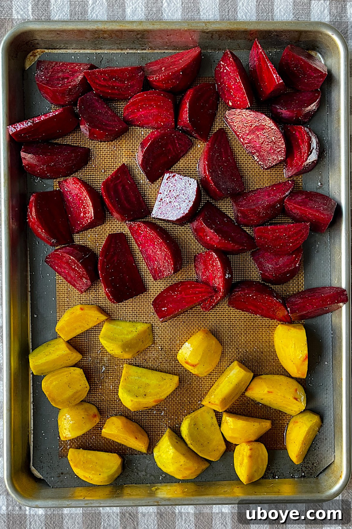 Sliced beet wedges seasoned with olive oil, salt, and pepper on a baking sheet lined with a silicone mat