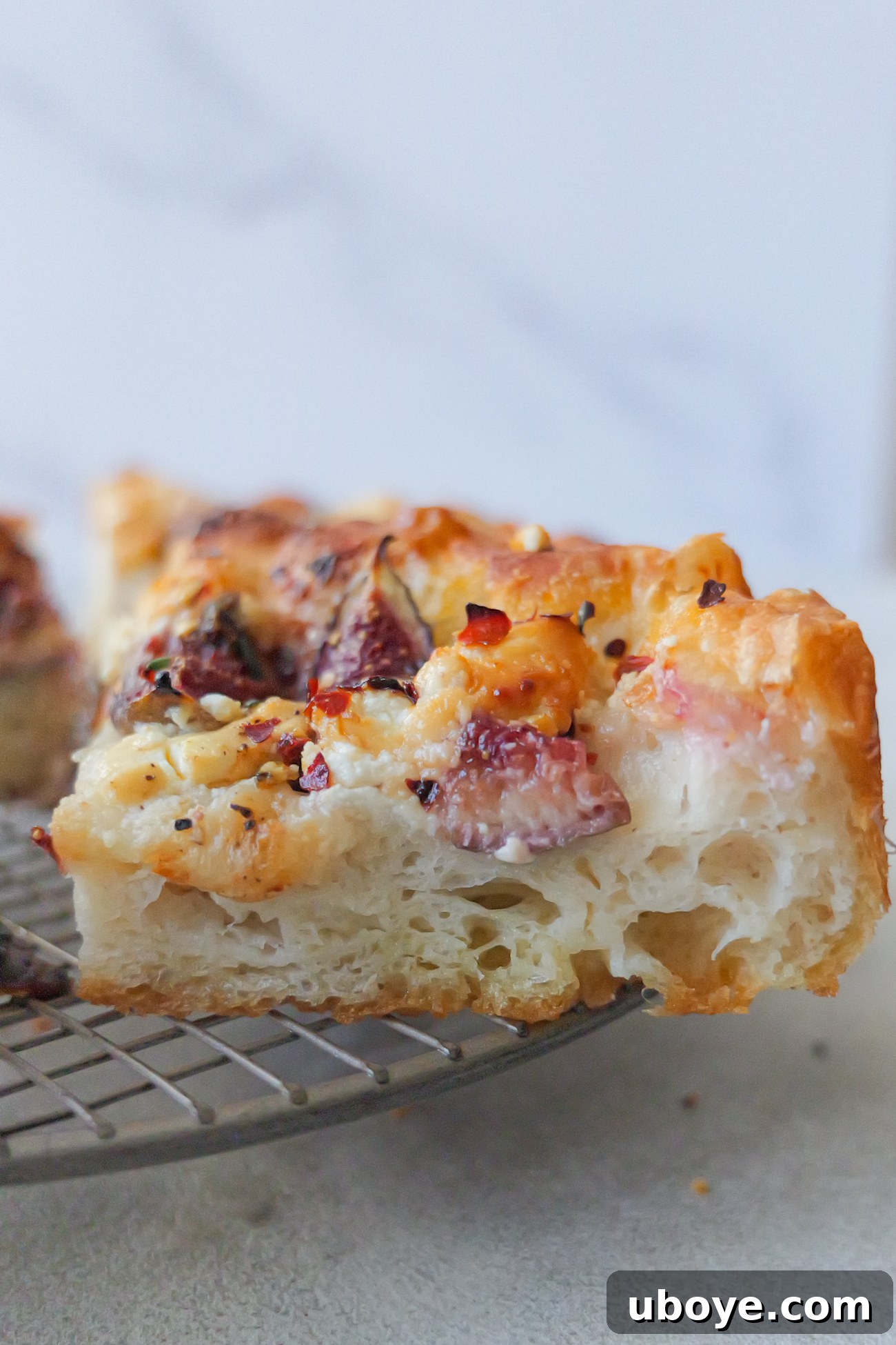 A delicious slice of fig and goat cheese focaccia artfully placed on a metal cooling rack, showcasing its inviting texture and toppings.