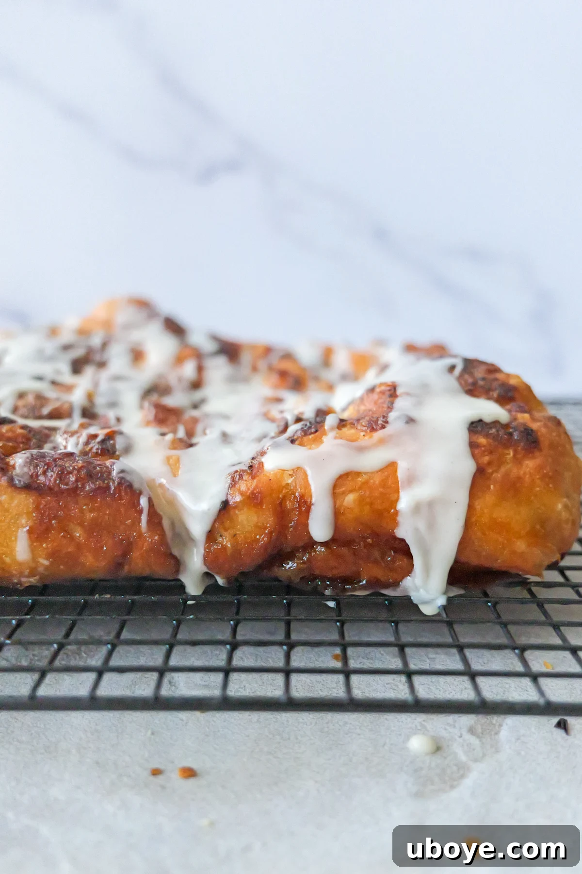 Cinnamon scroll sweet focaccia sits on a black wire rack, featuring a beautiful white glaze dripping elegantly off its golden edges.