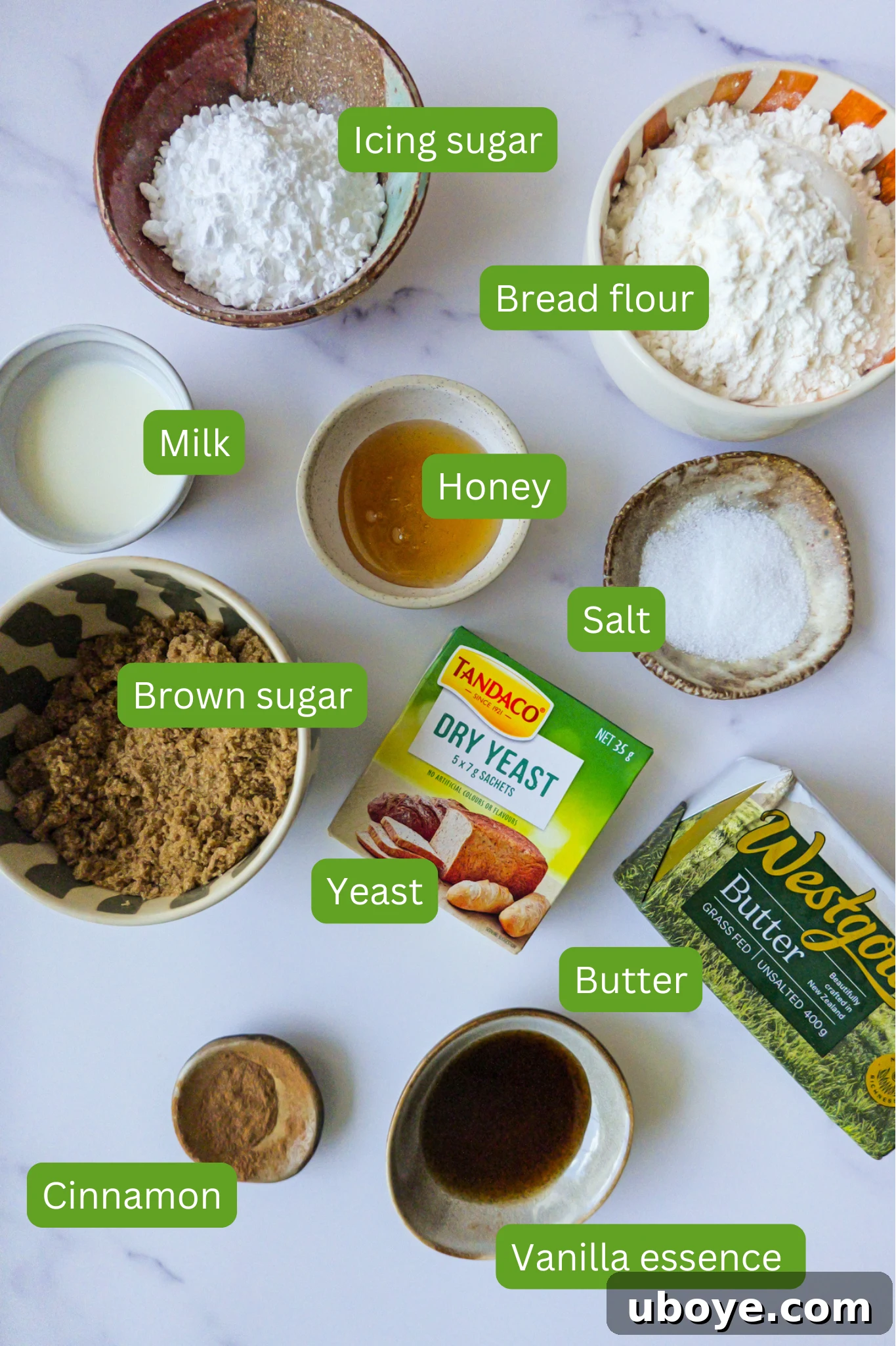 A flat lay image displaying all the necessary ingredients for crafting this delicious sweet cinnamon scroll focaccia. The collection includes blocks of butter, ground cinnamon, vanilla essence, active dry yeast, rich brown sugar, all-purpose flour, fine sea salt, golden honey, fresh milk, and powdered icing sugar, all neatly arranged.