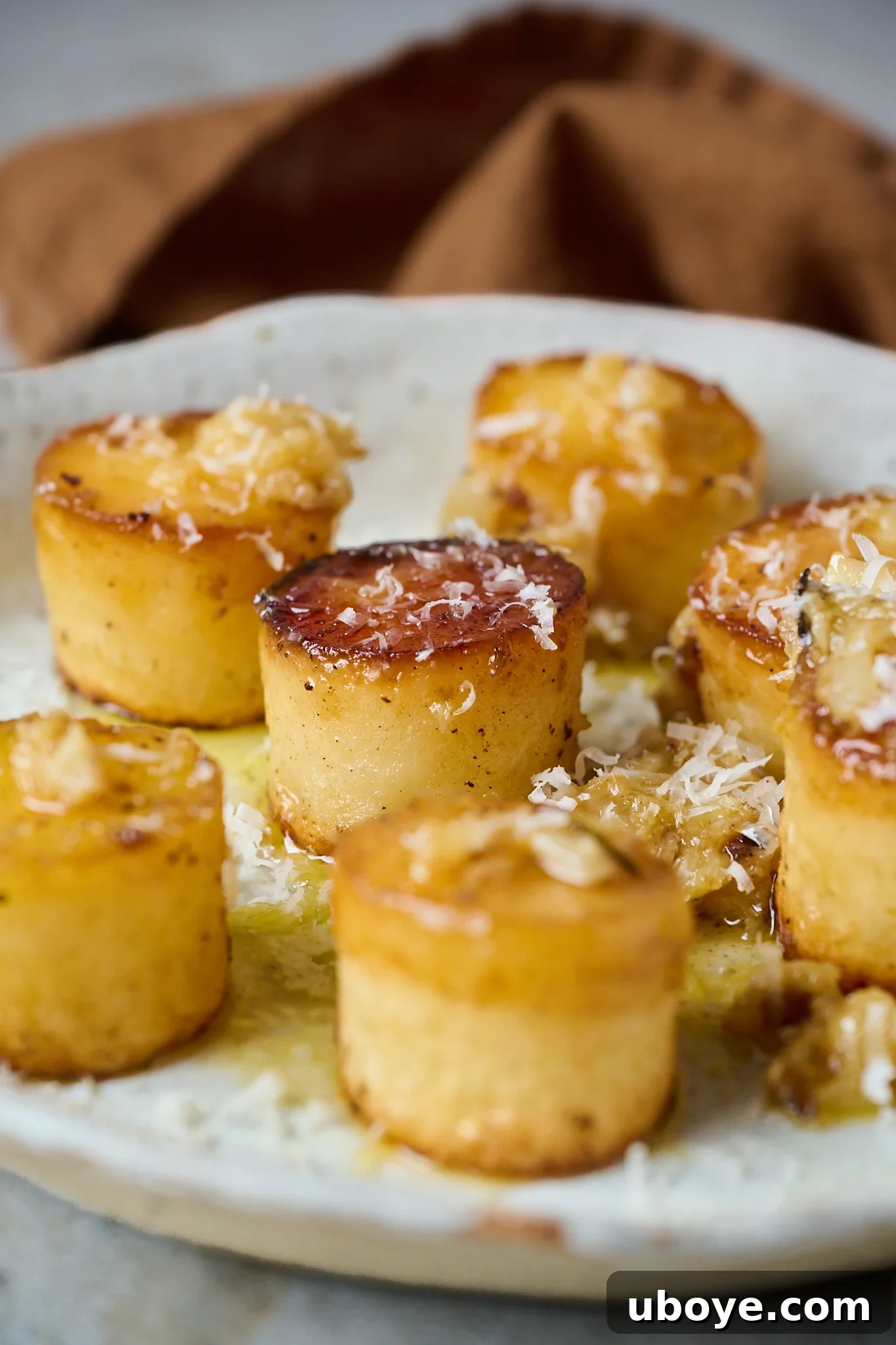 Golden Garlic Thyme Fondant Potatoes 2 Golden brown fondant potatoes served on a plate, generously drizzled with garlic butter and sprinkled with fresh parmesan cheese.