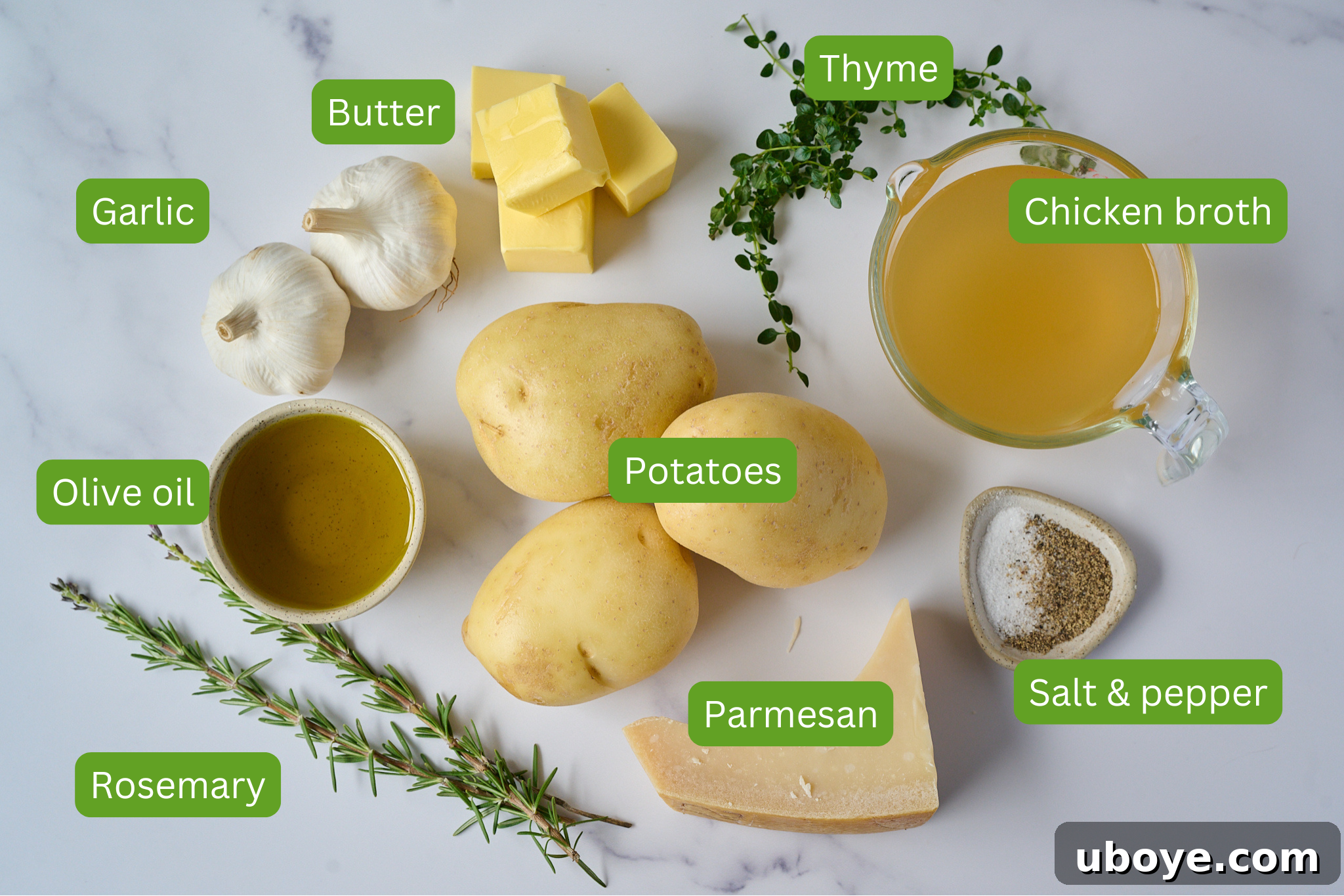 Golden Garlic Thyme Fondant Potatoes 3 A selection of fresh ingredients including butter, whole garlic bulbs, olive oil, fresh rosemary, fresh thyme, parmesan cheese, salt, pepper, and chicken broth laid out on a marble surface.