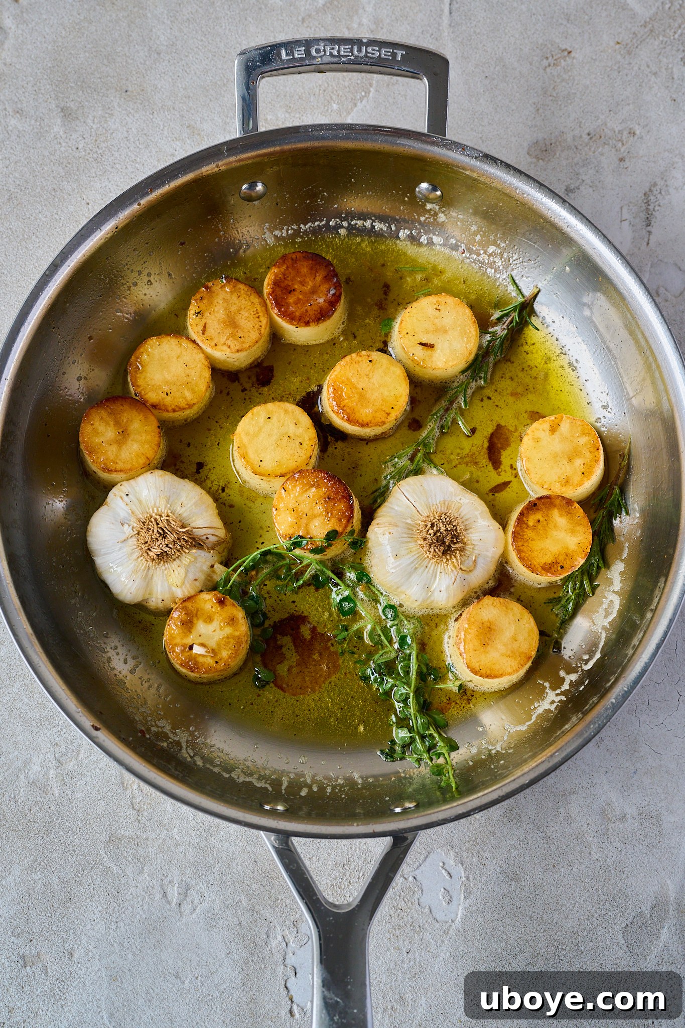 Golden Garlic Thyme Fondant Potatoes 6 Seared potatoes in a pan, surrounded by foaming butter, whole garlic bulbs, rosemary, and thyme sprigs.