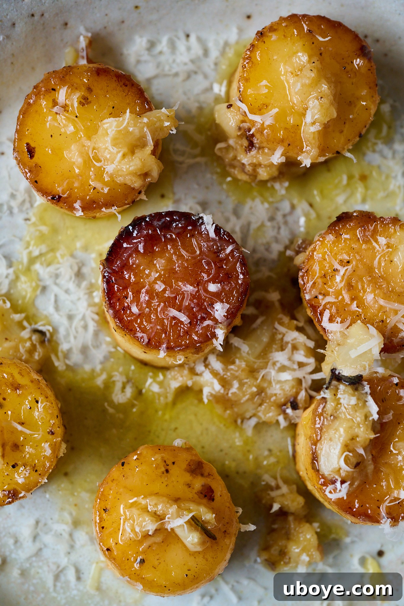 Golden Garlic Thyme Fondant Potatoes 7 Finished fondant potatoes on a plate, drenched in garlic butter sauce and garnished with fresh parmesan cheese.
