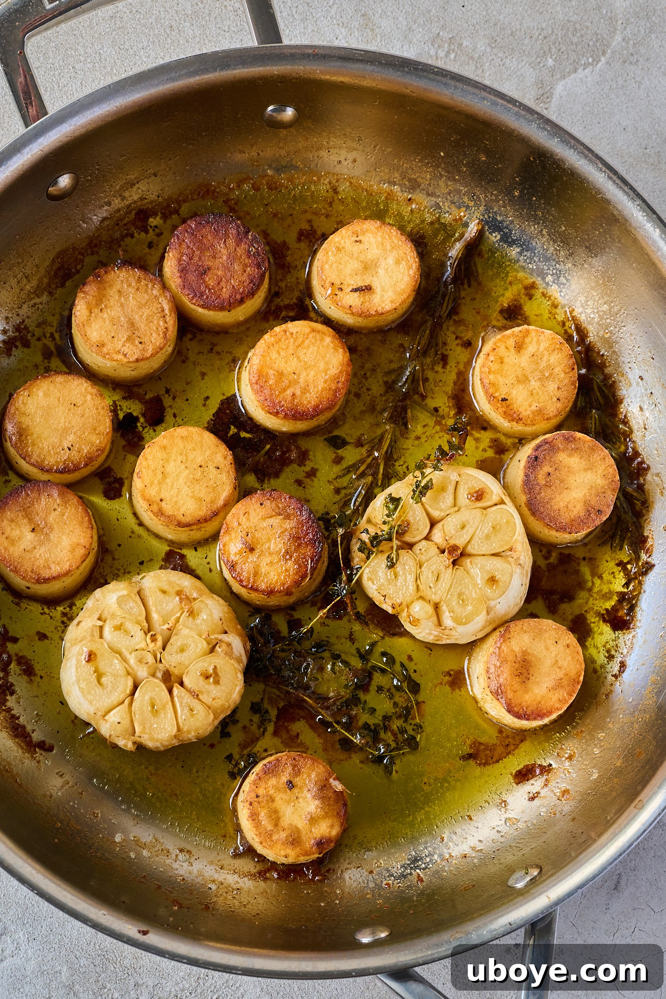 Golden Garlic Thyme Fondant Potatoes 8 Close-up of seared fondant potatoes cooking in a stainless steel pan with garlic, rosemary, and thyme in bubbling butter sauce.
