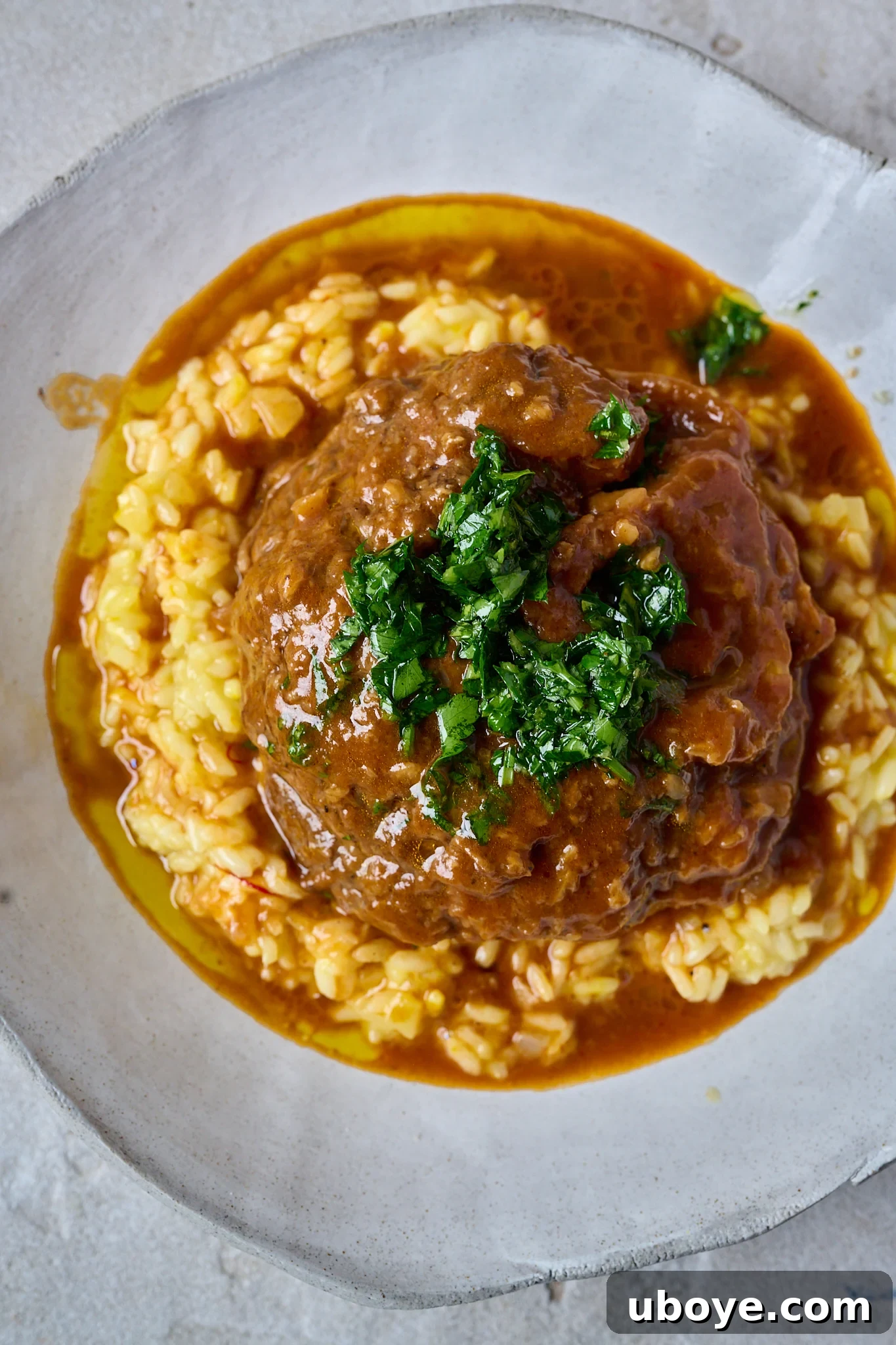 Braised Osso Buco with Zesty Gremolata and Creamy Risotto 2 A serving of Osso Buco on saffron risotto, garnished with fresh gremolata and rich sauce.