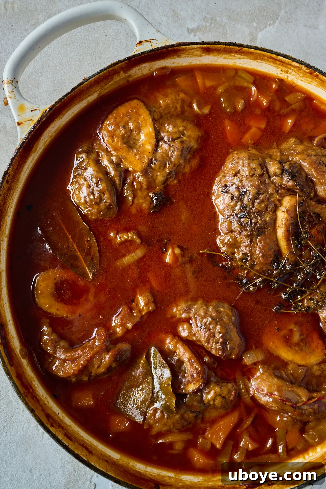 Braised Osso Buco with Zesty Gremolata and Creamy Risotto 8 Osso Buco braising in a rich red sauce with herbs in an oven-safe pot.