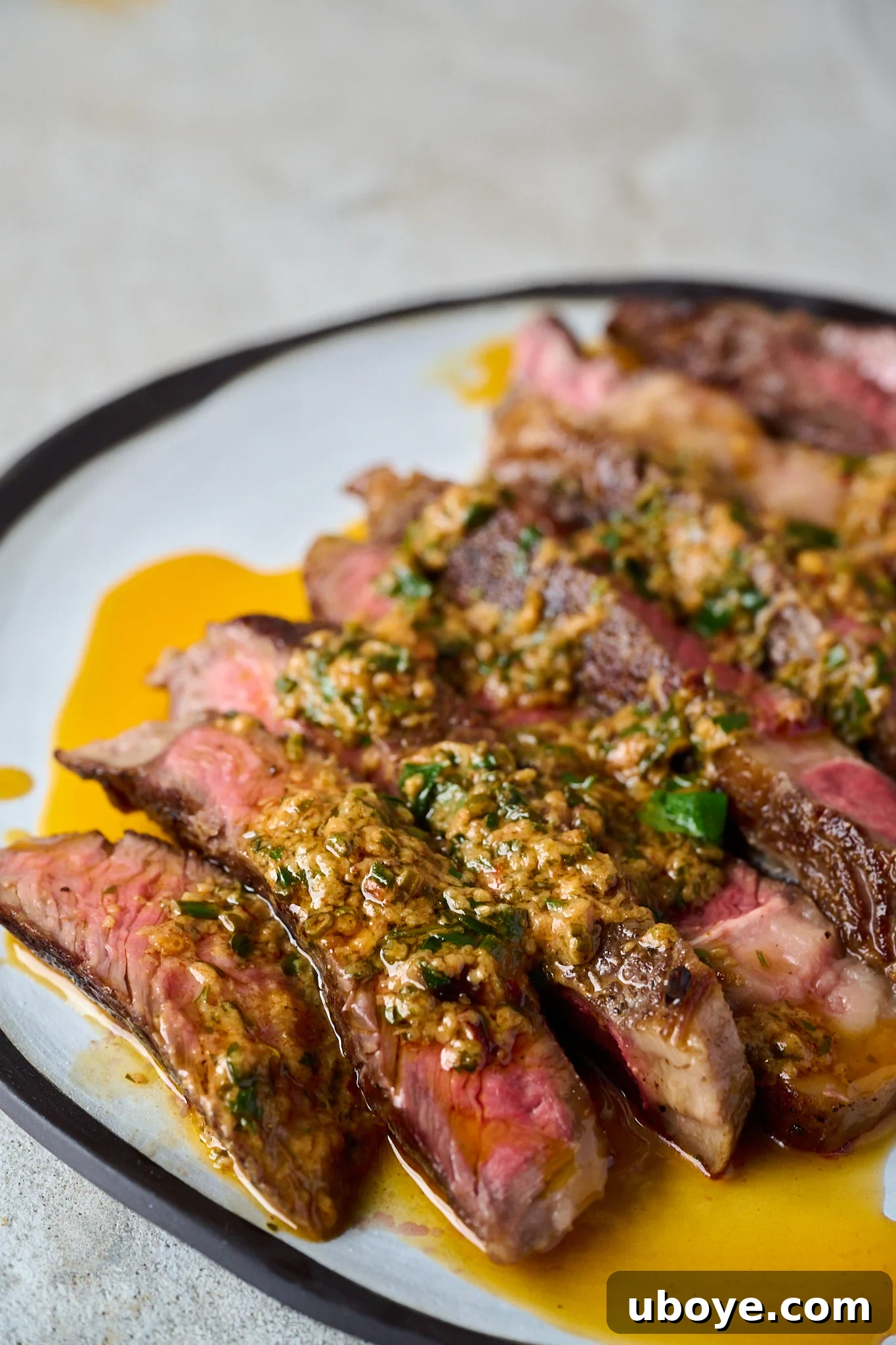 Cowboy butter has been drizzled onto sliced up steak that is sitting on a white plate with a black rim.