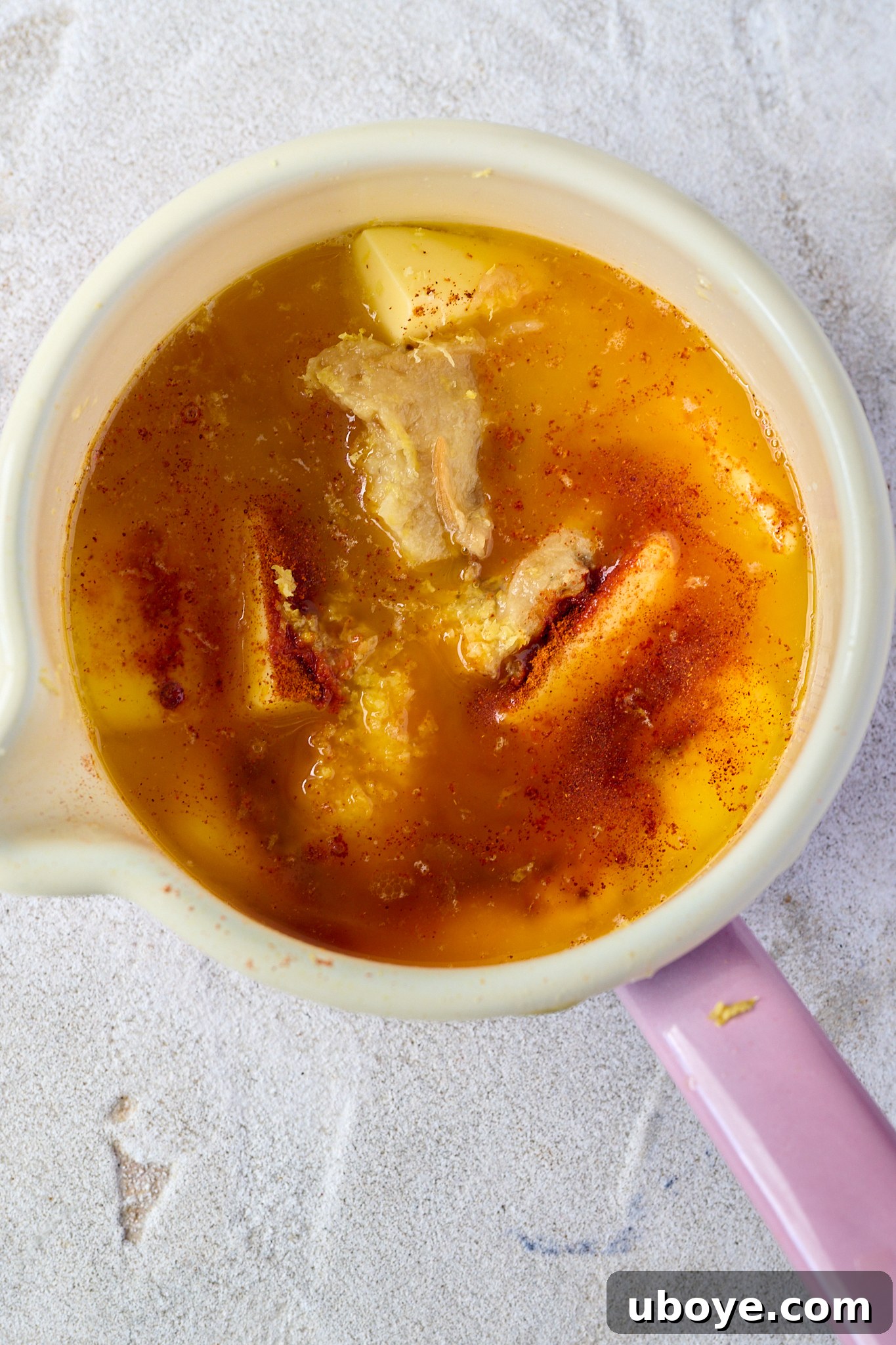 Butter and spices melting in a white pot with a pink handle on a stovetop.