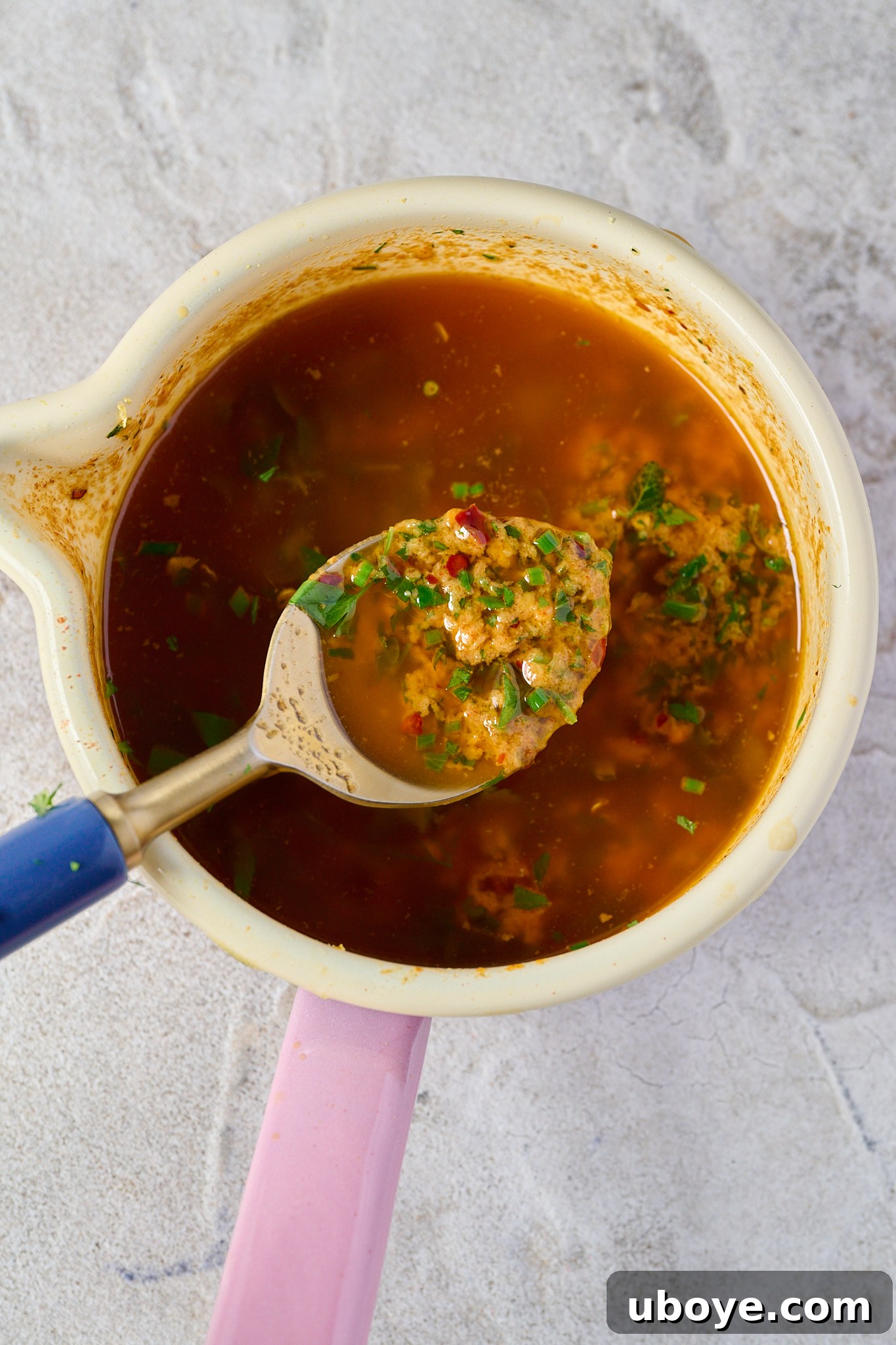 Melted butter with spices and fresh herbs mixed in, sitting in a white bowl with a pink handle.