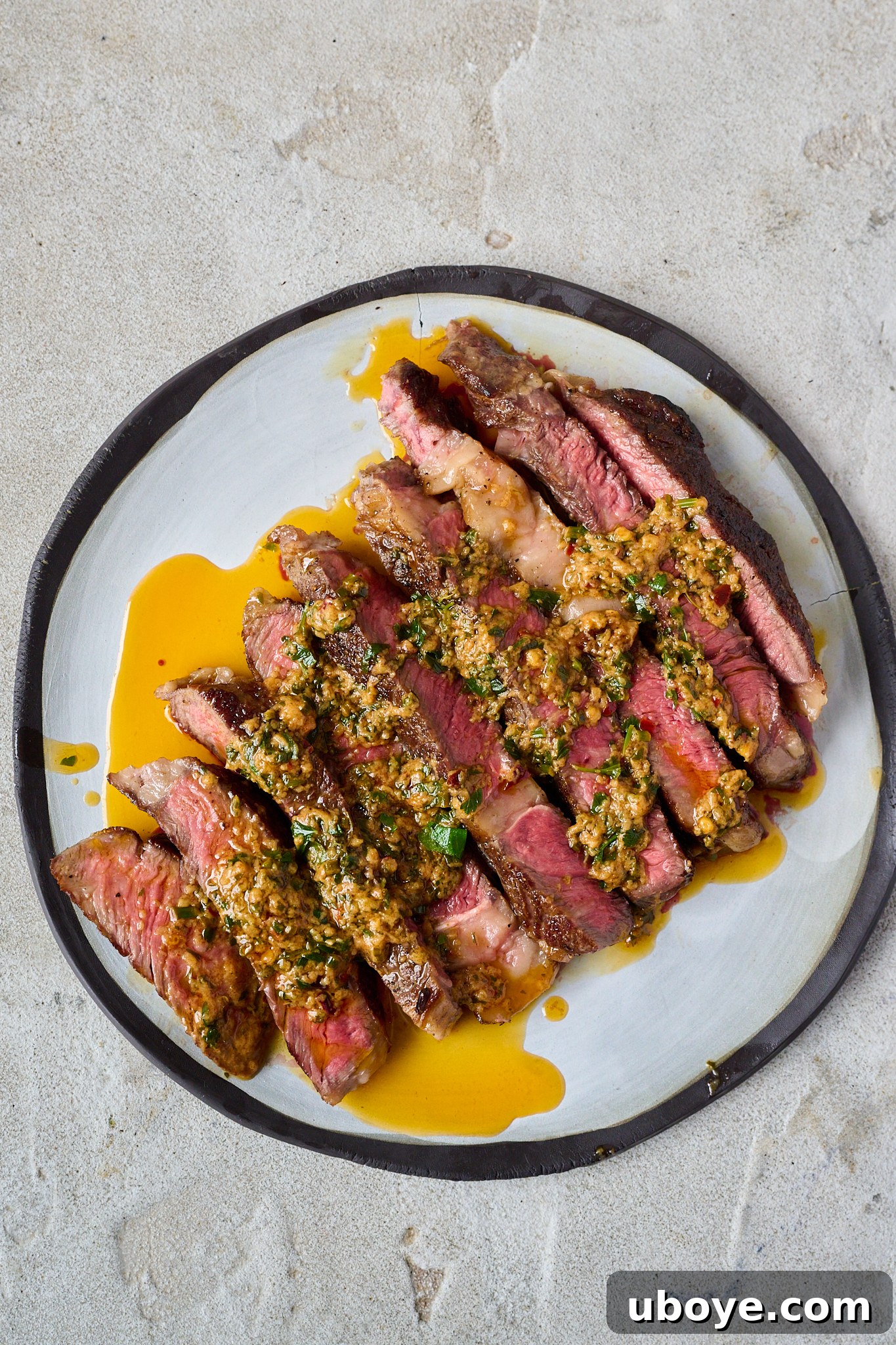 Cowboy butter has been drizzled onto sliced up steak that is sitting on a white plate with a black rim.