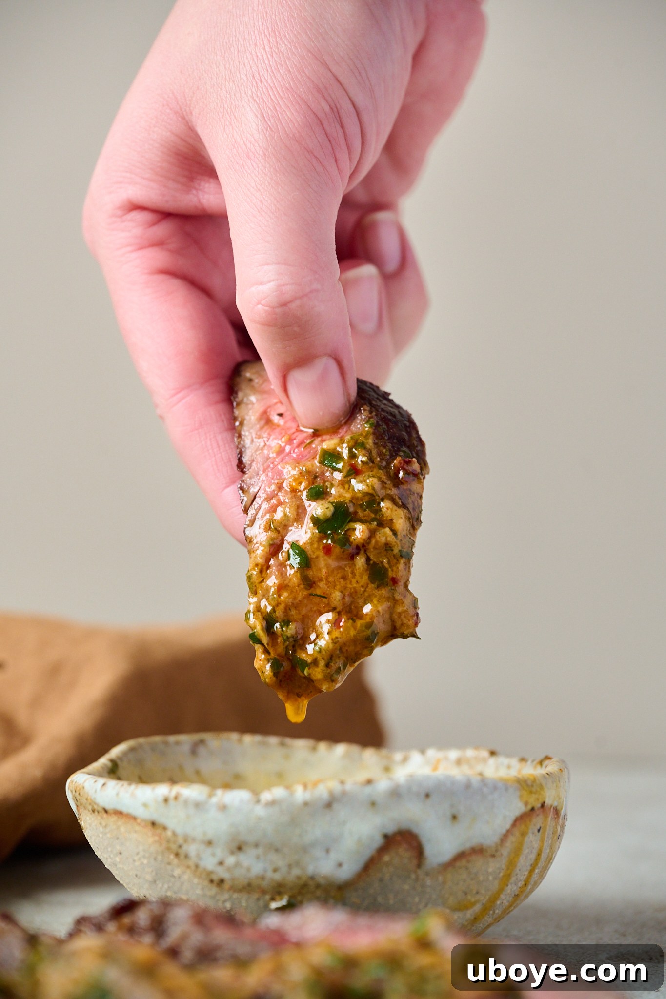 A piece of steak is being held up between someone's fingers and is being dipped into the cowboy butter that is in a small white bowl.