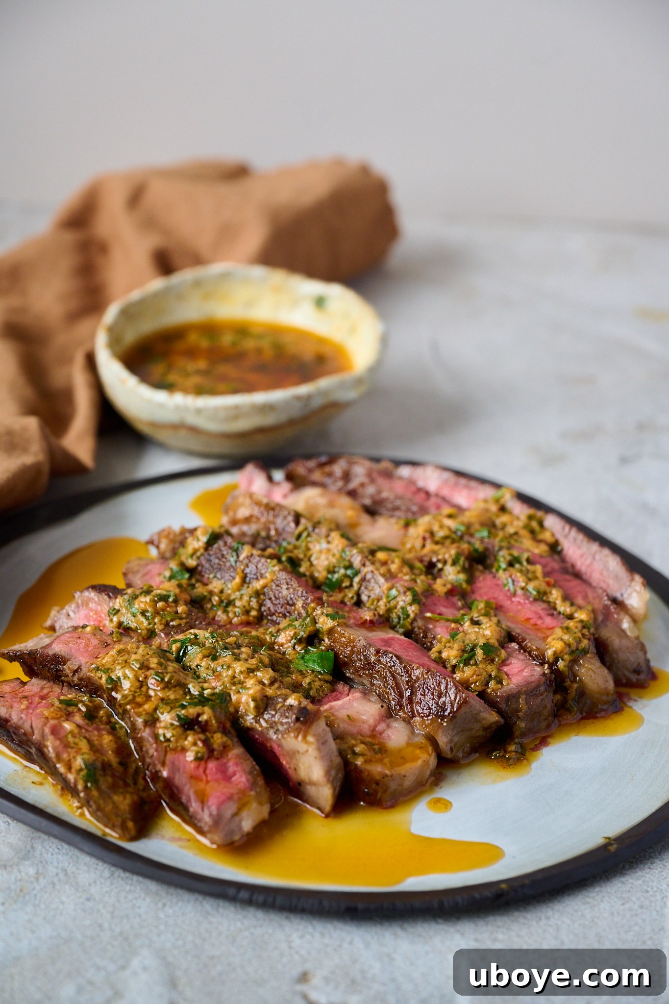 Cowboy butter has been drizzled onto sliced up steak that is sitting on a white plate with a black rim.