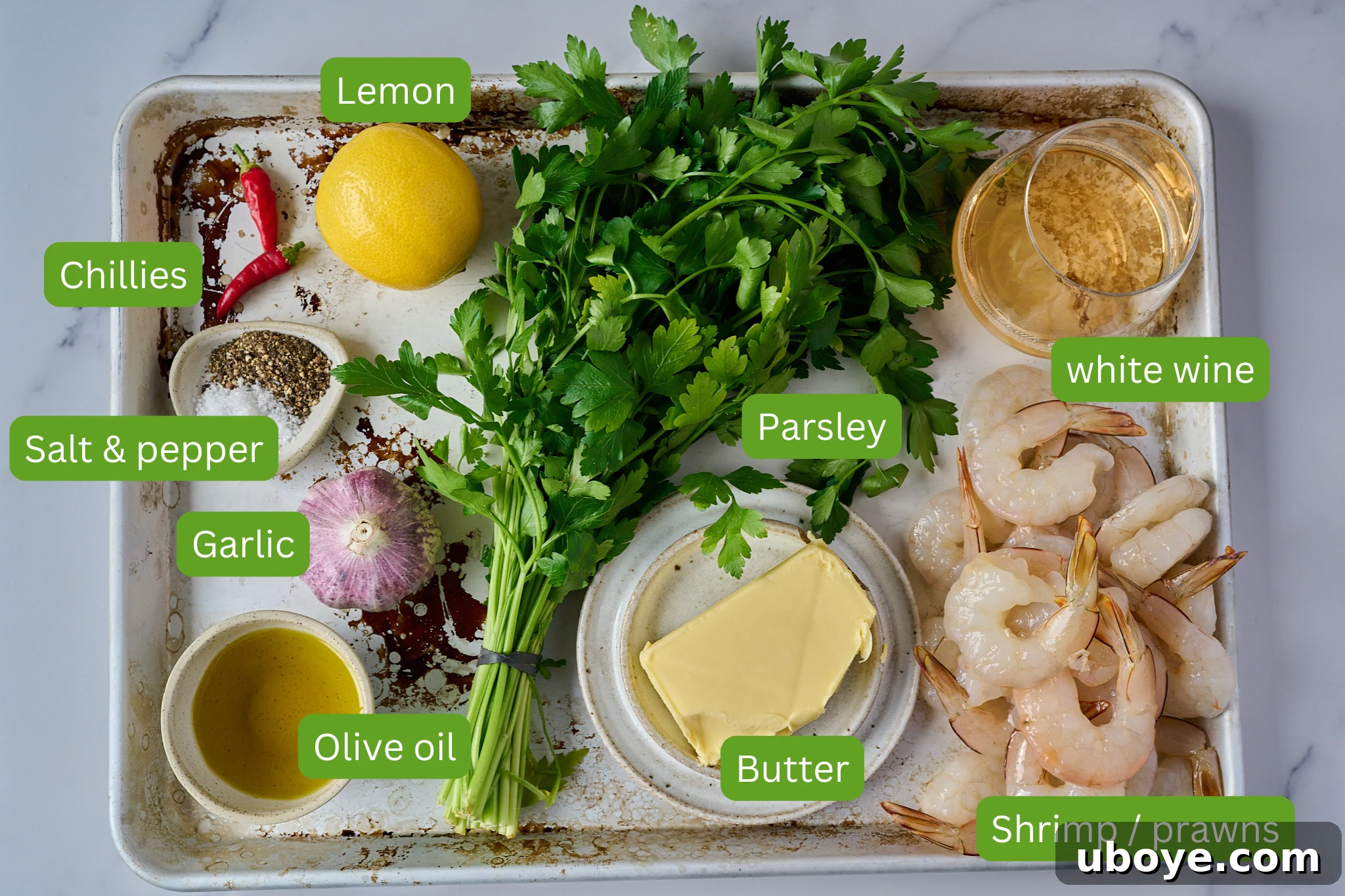 Ingredients for garlic butter prawns / shrimp laid out on a metal tray, including fresh shrimp, garlic cloves, butter, olive oil, white wine, lemon, chili flakes, salt, and pepper.