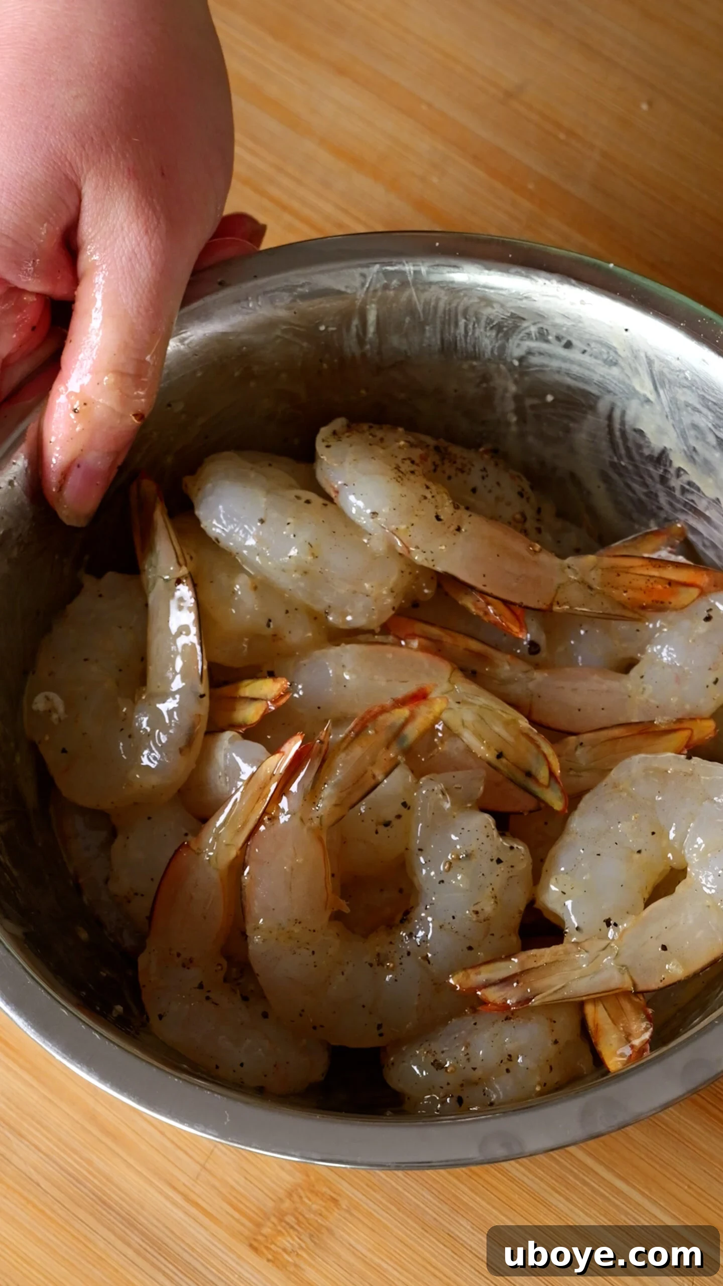 Raw shrimp seasoned with salt, pepper, and olive oil in a stainless steel bowl, ready for searing.