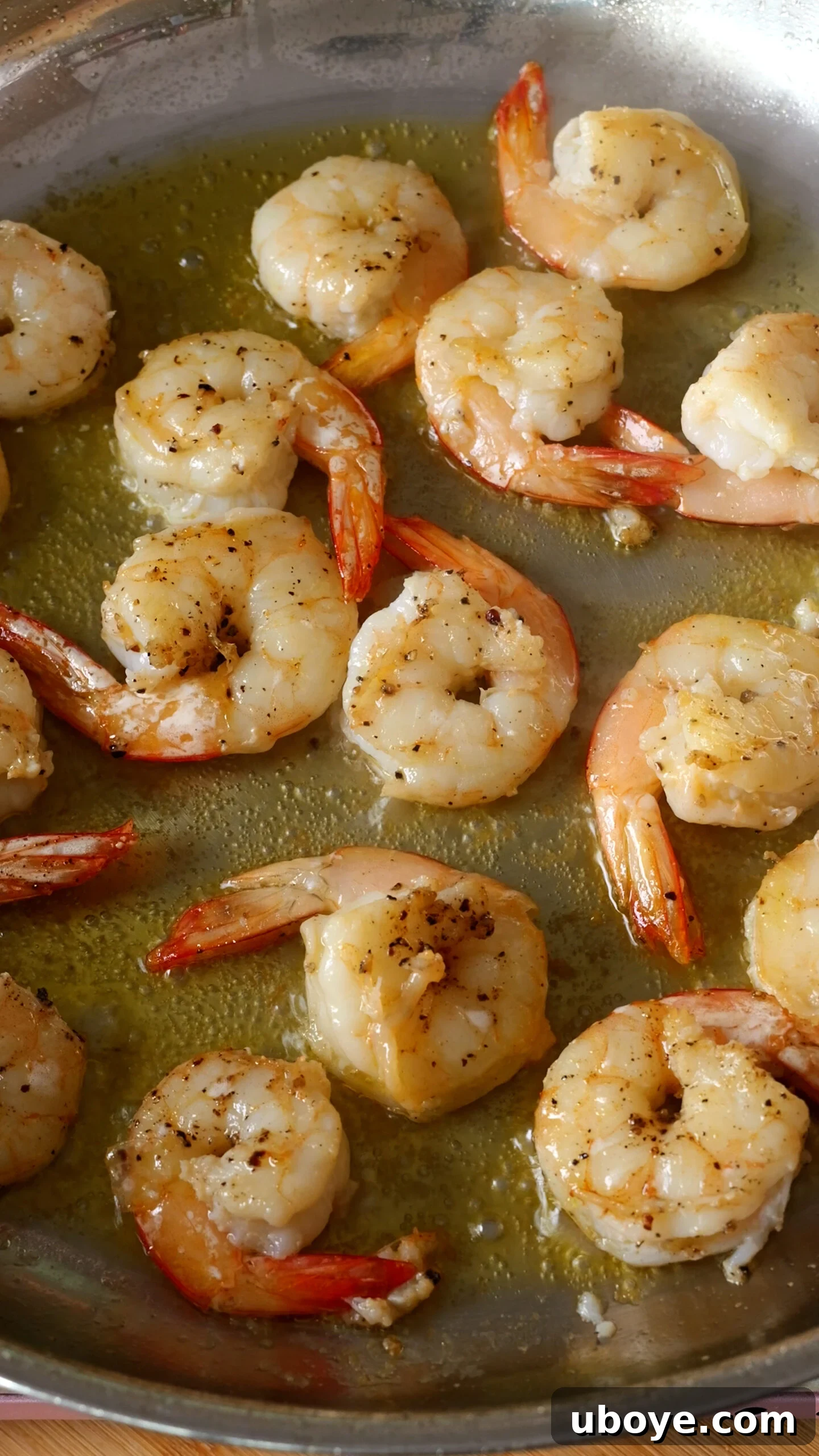 Shrimp searing in a stainless steel pan, turning pink and curling slightly.