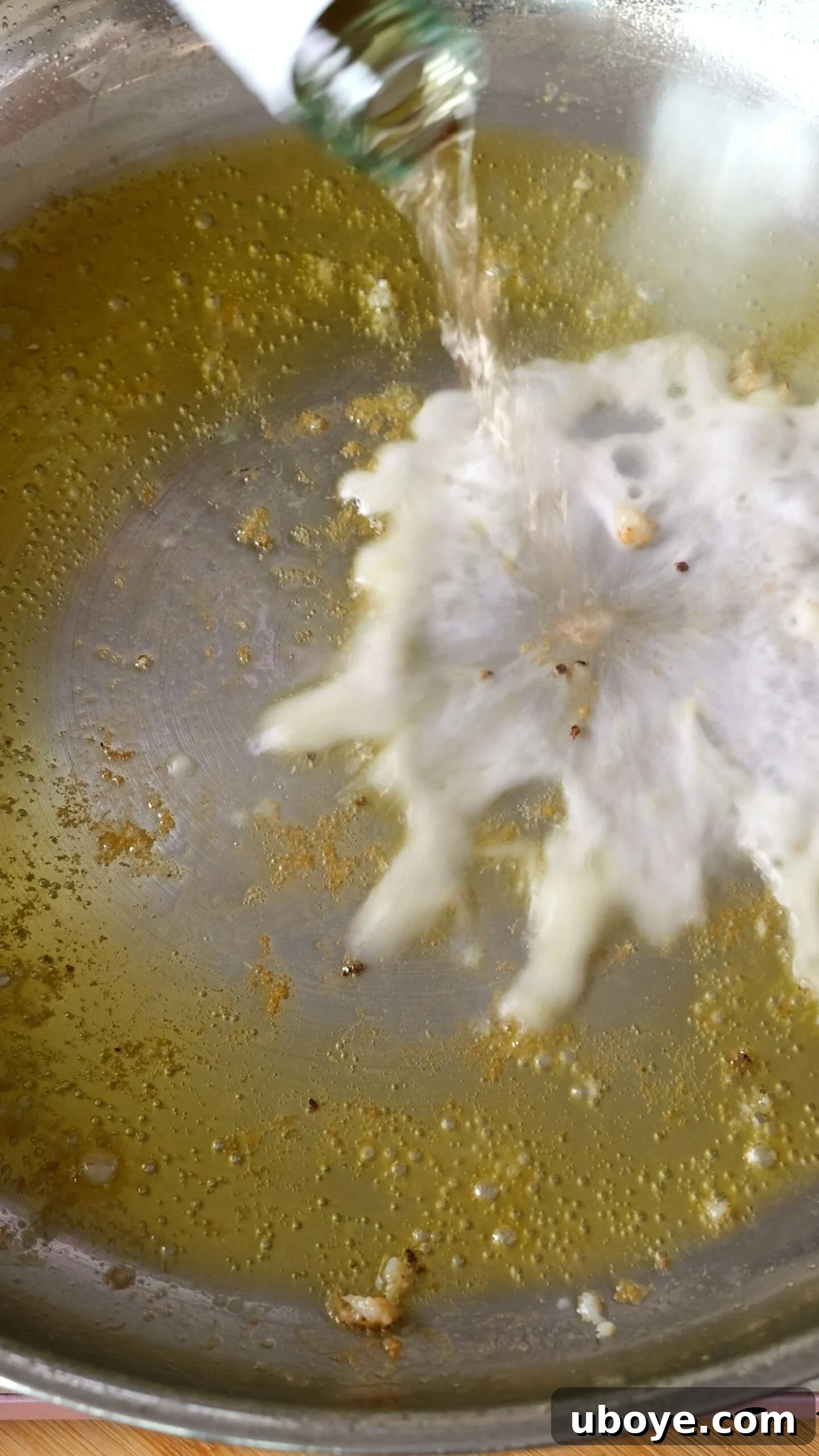 White wine being poured into the hot pan to deglaze after the shrimp have been removed.