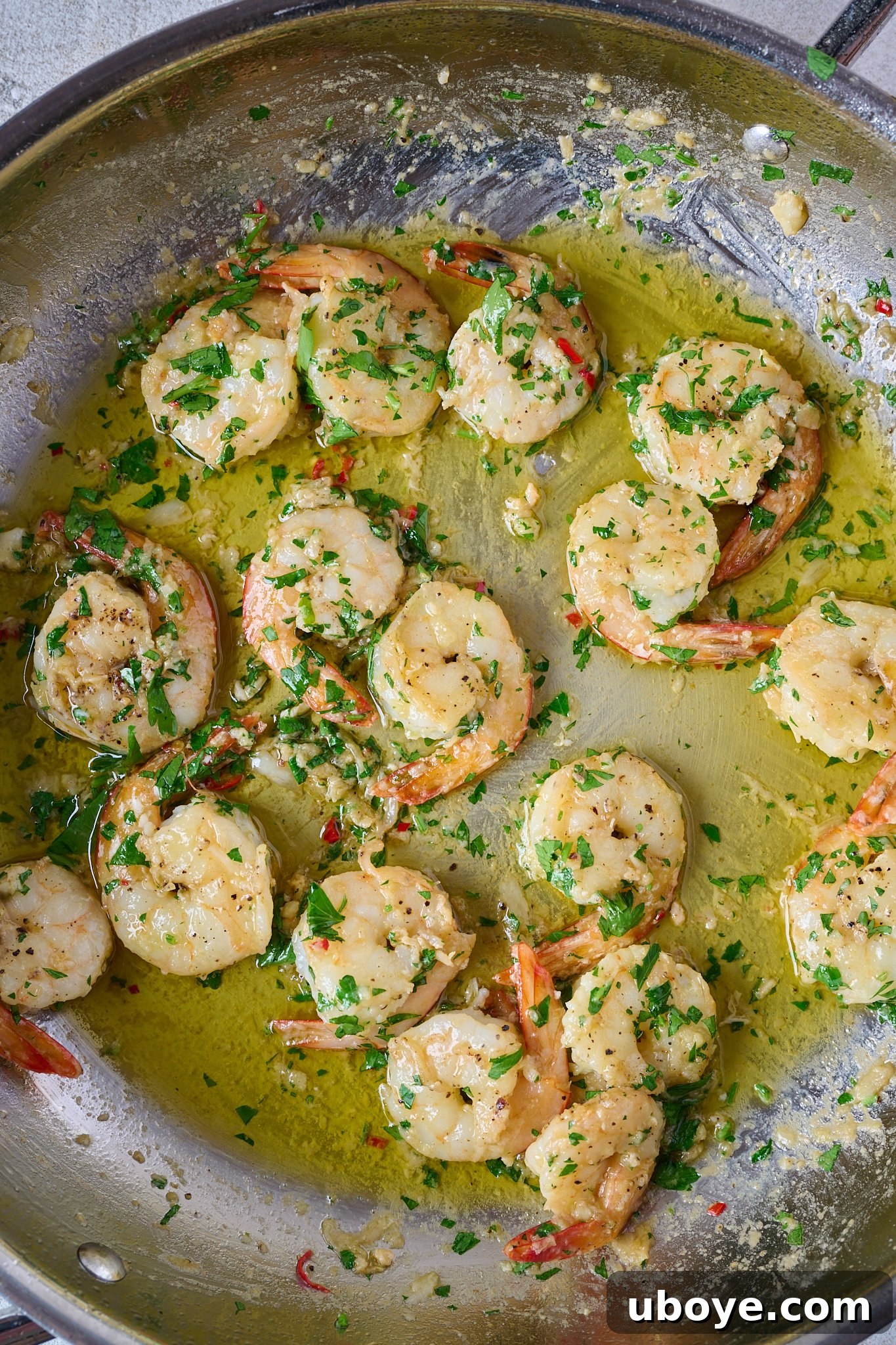 Garlic butter prawns / shrimp coated in sauce in a stainless steel pan, finished with fresh parsley.