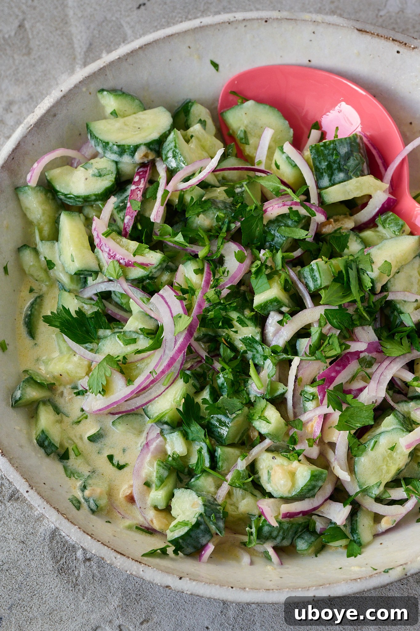 Zesty Greek Yogurt Cucumber Salad 2 Large white bowl filled with creamy cucumber salad with Greek yogurt, a pink spoon rests on the side.