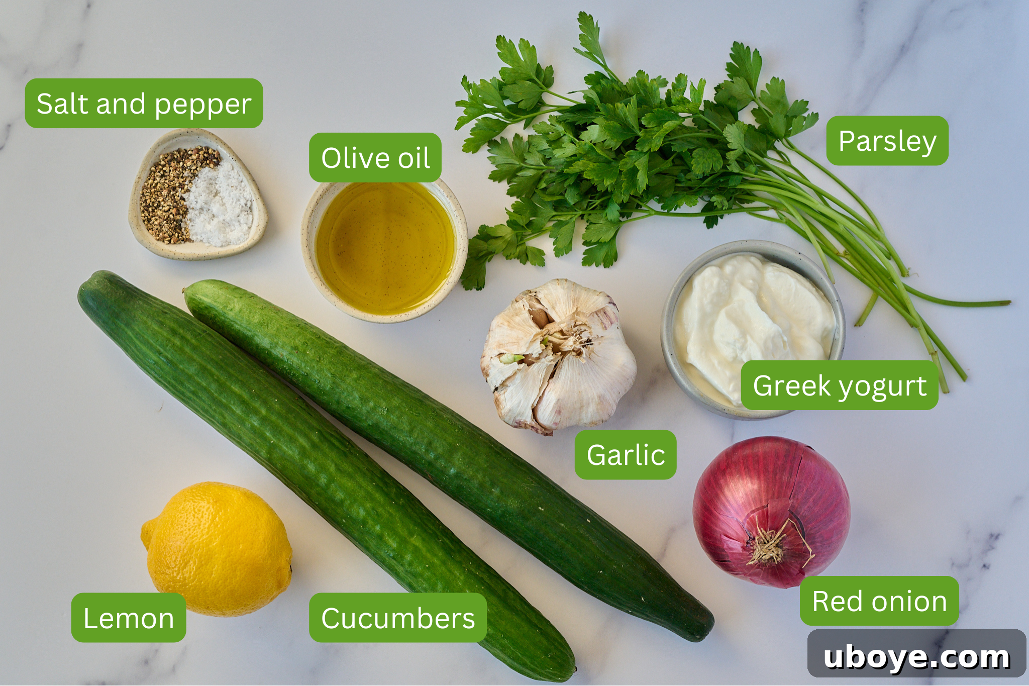 Zesty Greek Yogurt Cucumber Salad 3 Arrangement of ingredients for creamy cucumber salad on a marble surface, including cucumbers, lemon, garlic, red onion, Greek yogurt, fresh parsley, olive oil, and salt and pepper.