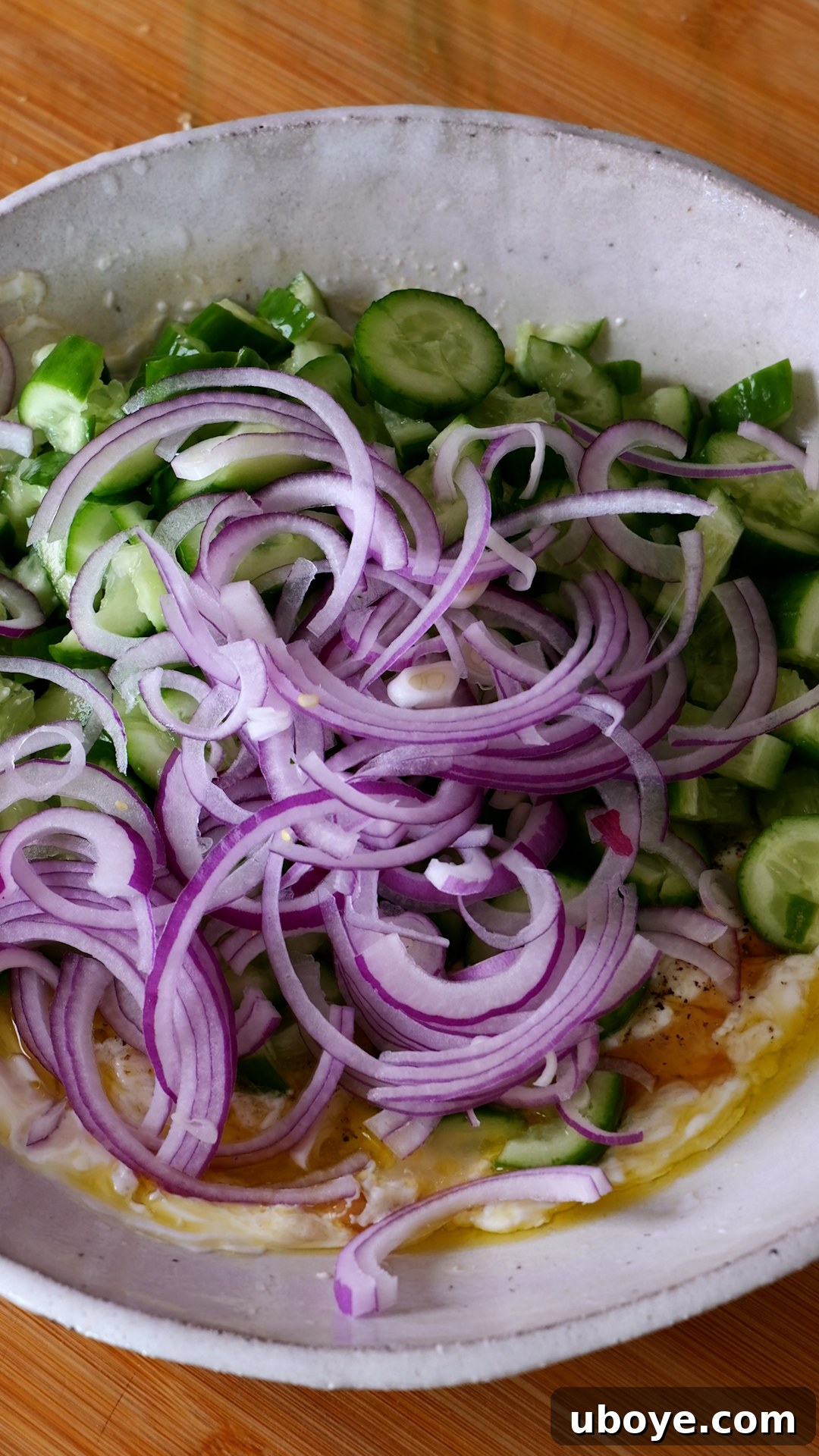 Zesty Greek Yogurt Cucumber Salad 5 Bowl with prepared dressing, now with cucumbers and red onion added, ready to be mixed.