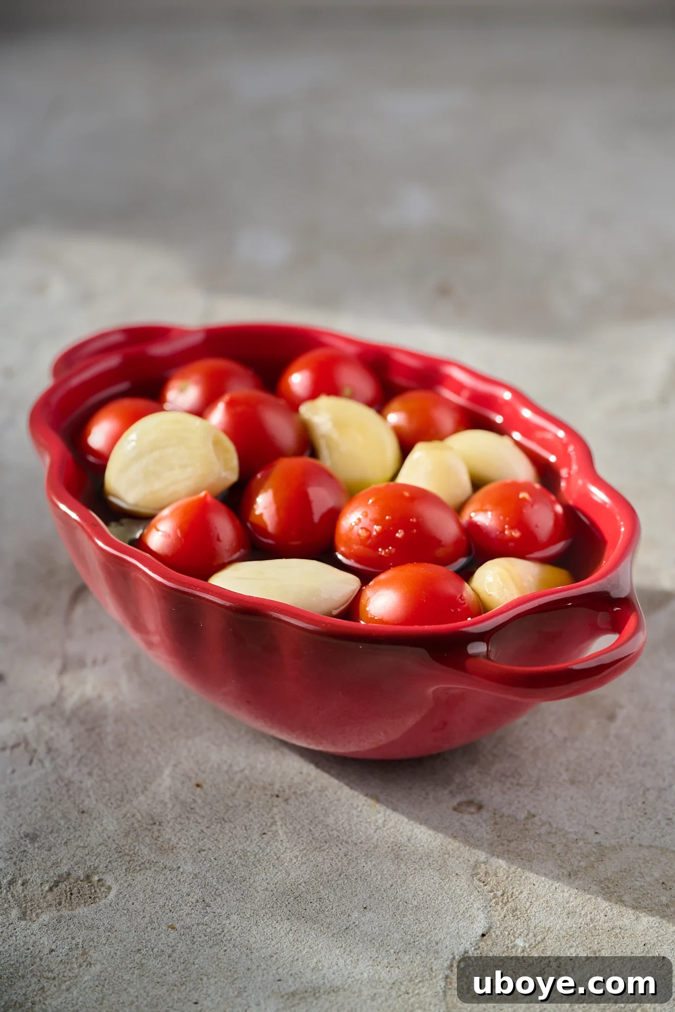 Tomatoes and garlic cloves sit in a red pot.