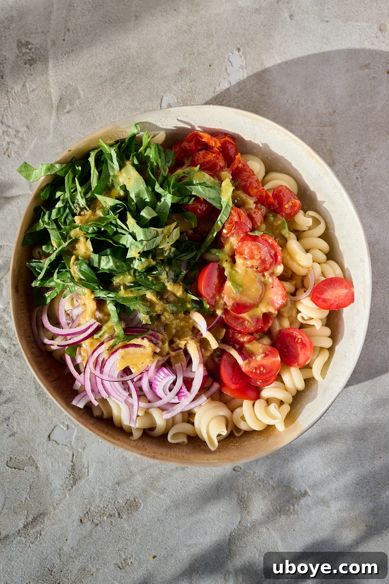 Mediterranean Tomato Confit Pasta Salad sits in large bowl in the sun. There are fresh basil leaves and chilli flakes sprinkled on top.