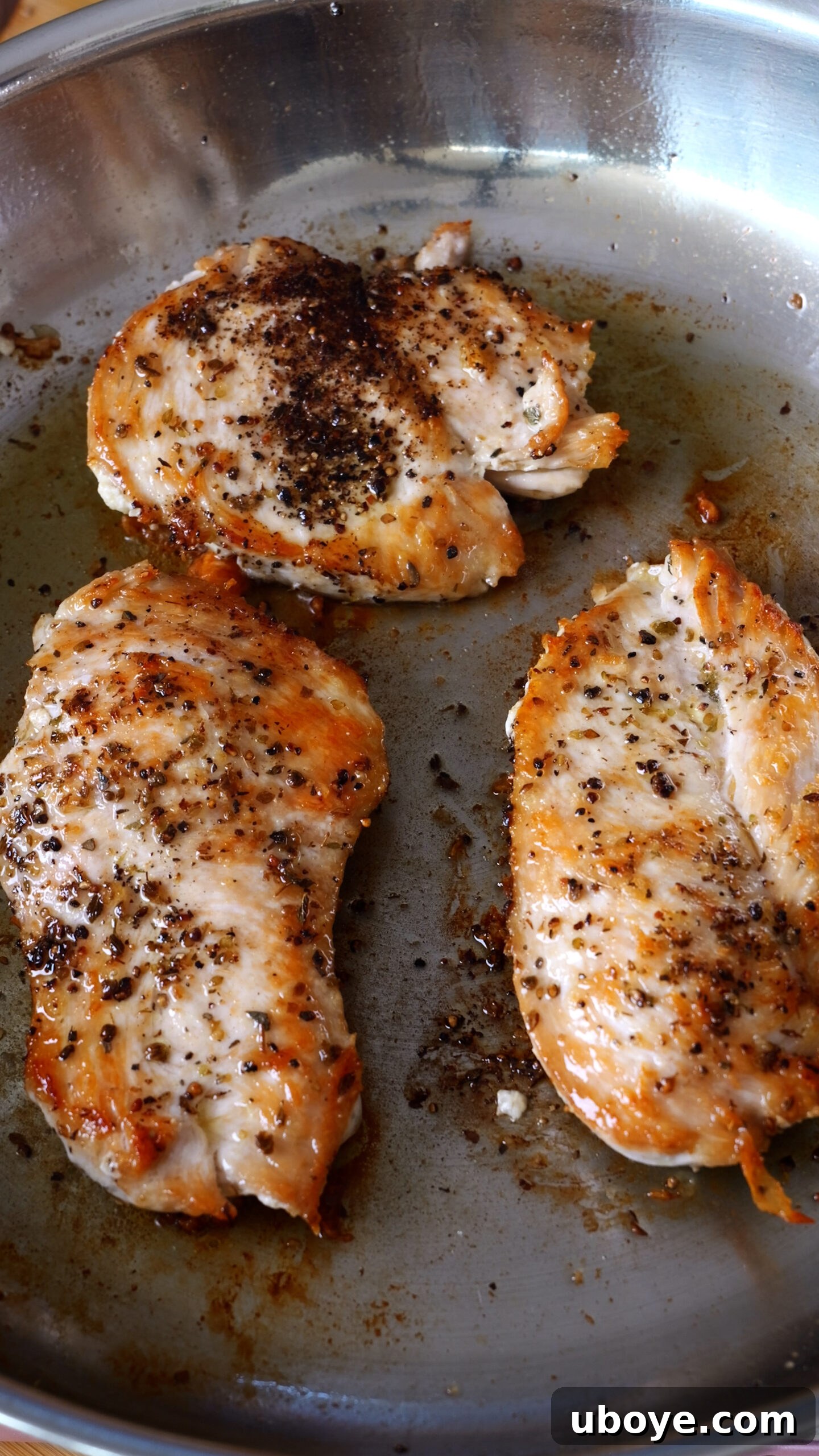 Seared chicken is seen in stainless steel pan.