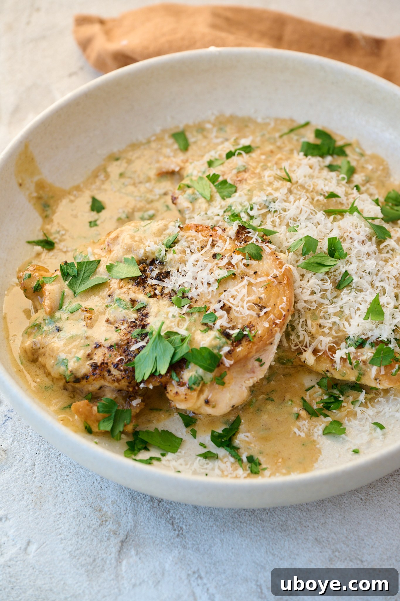 Creamy garlic parmesan chicken is served in white plate with fresh parsley and cheese sprinkled on top.