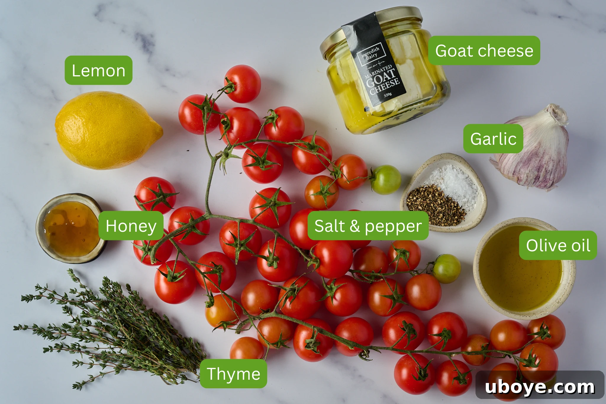 A beautiful flat lay of fresh ingredients including vibrant cherry tomatoes on the vine, a bulb of garlic, a block of creamy goat cheese, a fresh lemon, a bottle of olive oil, a jar of honey, and fresh thyme sprigs, all ready for the recipe.