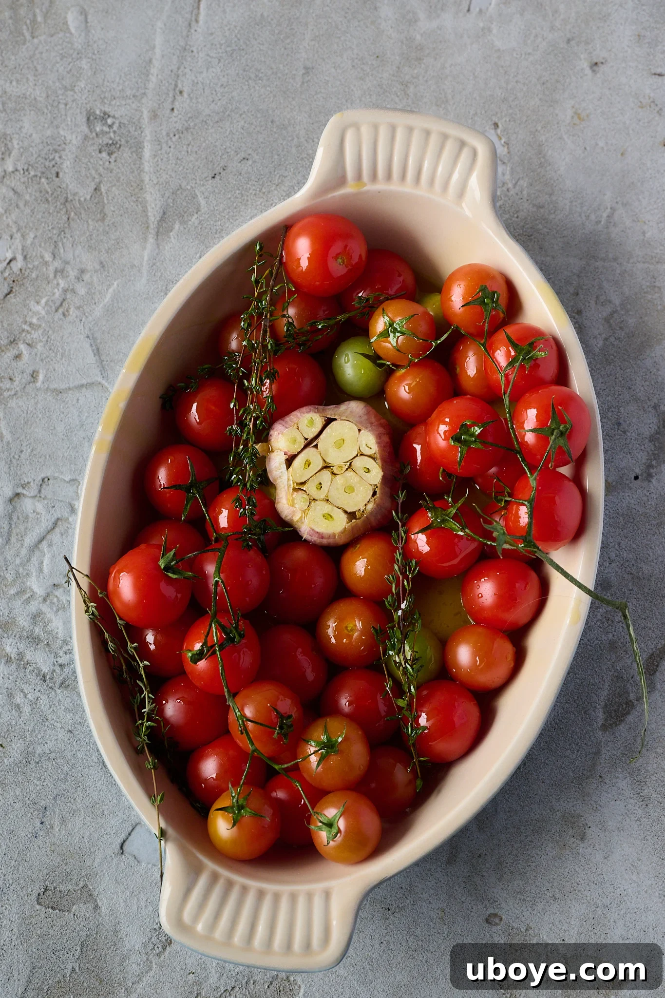 A large roasting dish brimming with fresh cherry tomatoes and a whole garlic bulb, drizzled with olive oil and ready for the oven.