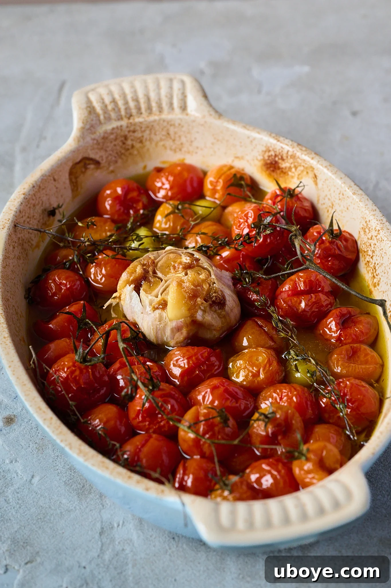 A large roasting dish containing beautifully baked cherry tomatoes, now softened and slightly burst, alongside a golden-brown roasted garlic bulb.