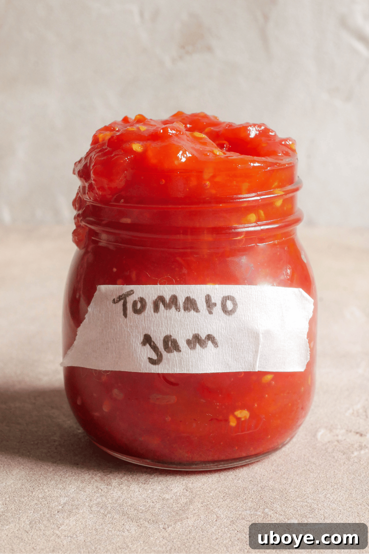 A beautifully labeled glass jar of homemade tomato jam, sealed and ready for refrigeration or gifting, capturing the vibrant red color of the preserve.