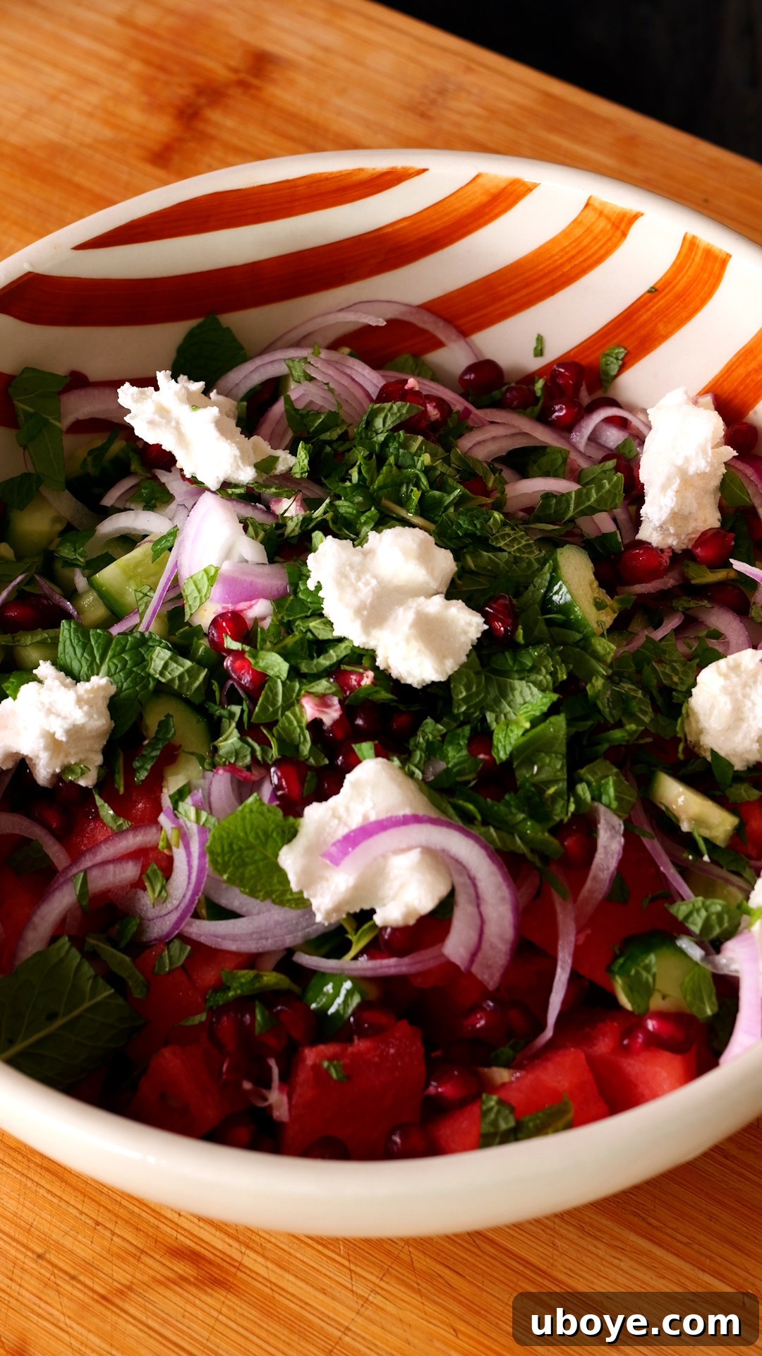 Crisp Watermelon, Feta & Cucumber Medley 5 A large orange and white striped bowl containing all the prepared salad ingredients, perfectly cubed watermelon, sliced cucumber, crumbled feta, and fresh mint.