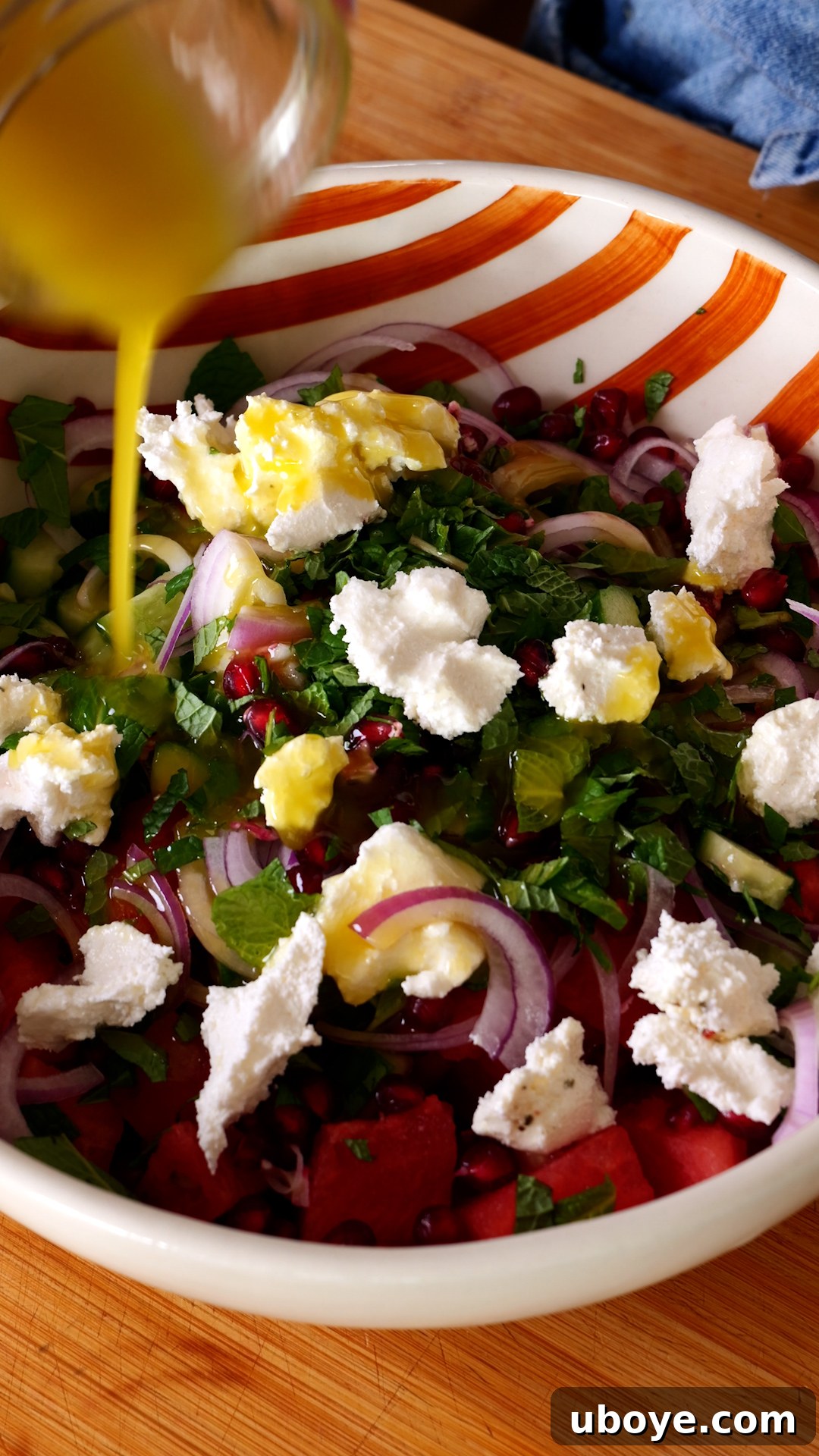 Crisp Watermelon, Feta & Cucumber Medley 6 The vibrant salad ingredients in a large orange and white striped bowl, with the prepared dressing being drizzled generously over them.