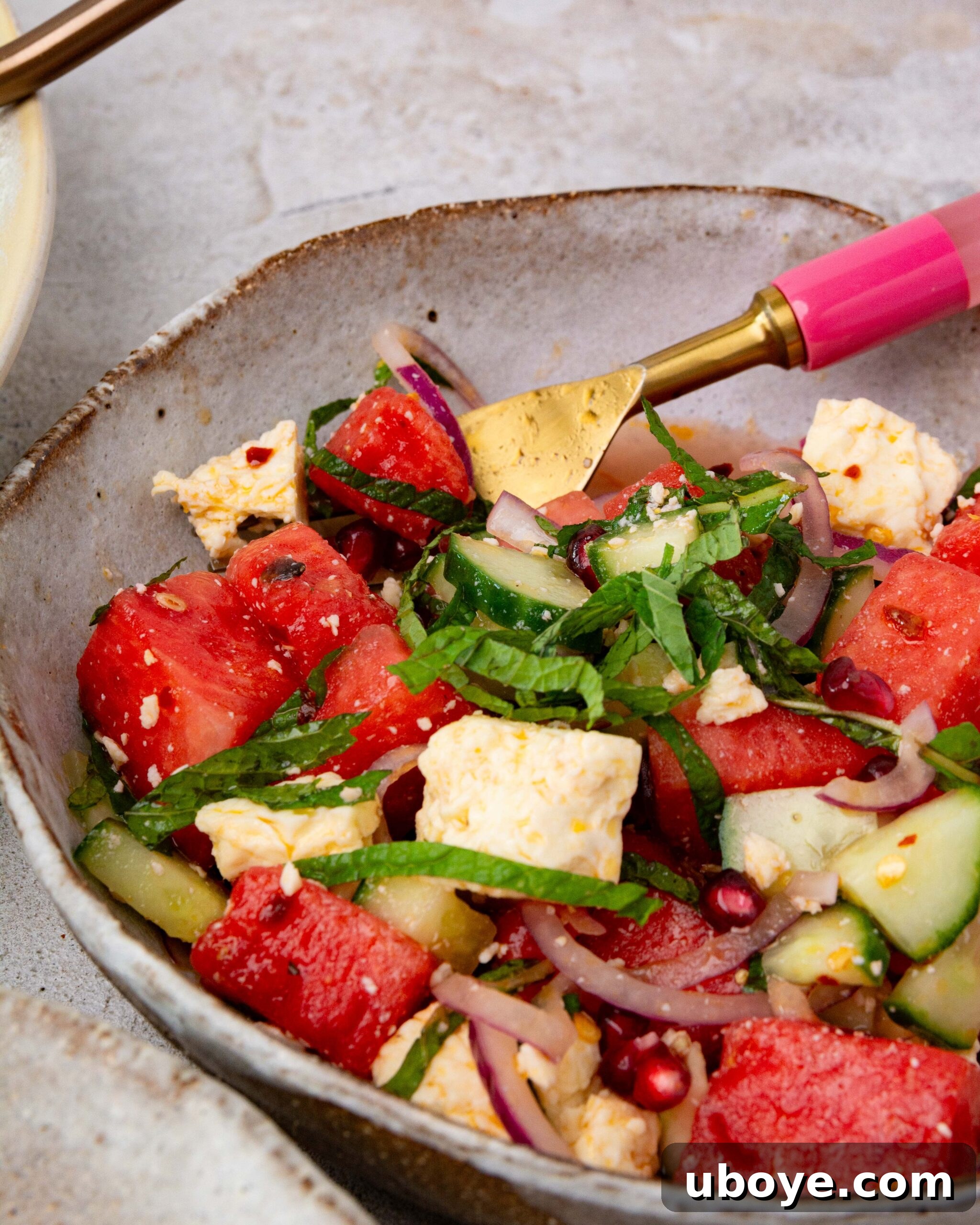 Crisp Watermelon, Feta & Cucumber Medley 7 A small brown bowl holding a serving of Feta, Watermelon & Cucumber Salad, garnished with mint, with a pink fork resting beside it, ready to be enjoyed.