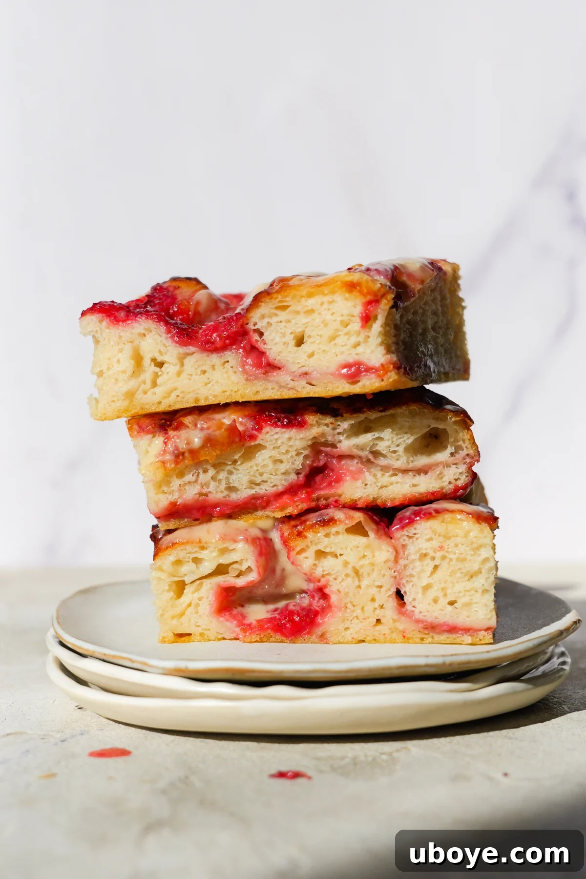Sweet Focaccia with Strawberry Jam and Cream Cheese Glaze 2 Three slices of strawberry jam sweet focaccia are sitting on top of each other and are placed on three white plates also sitting on top of one another.