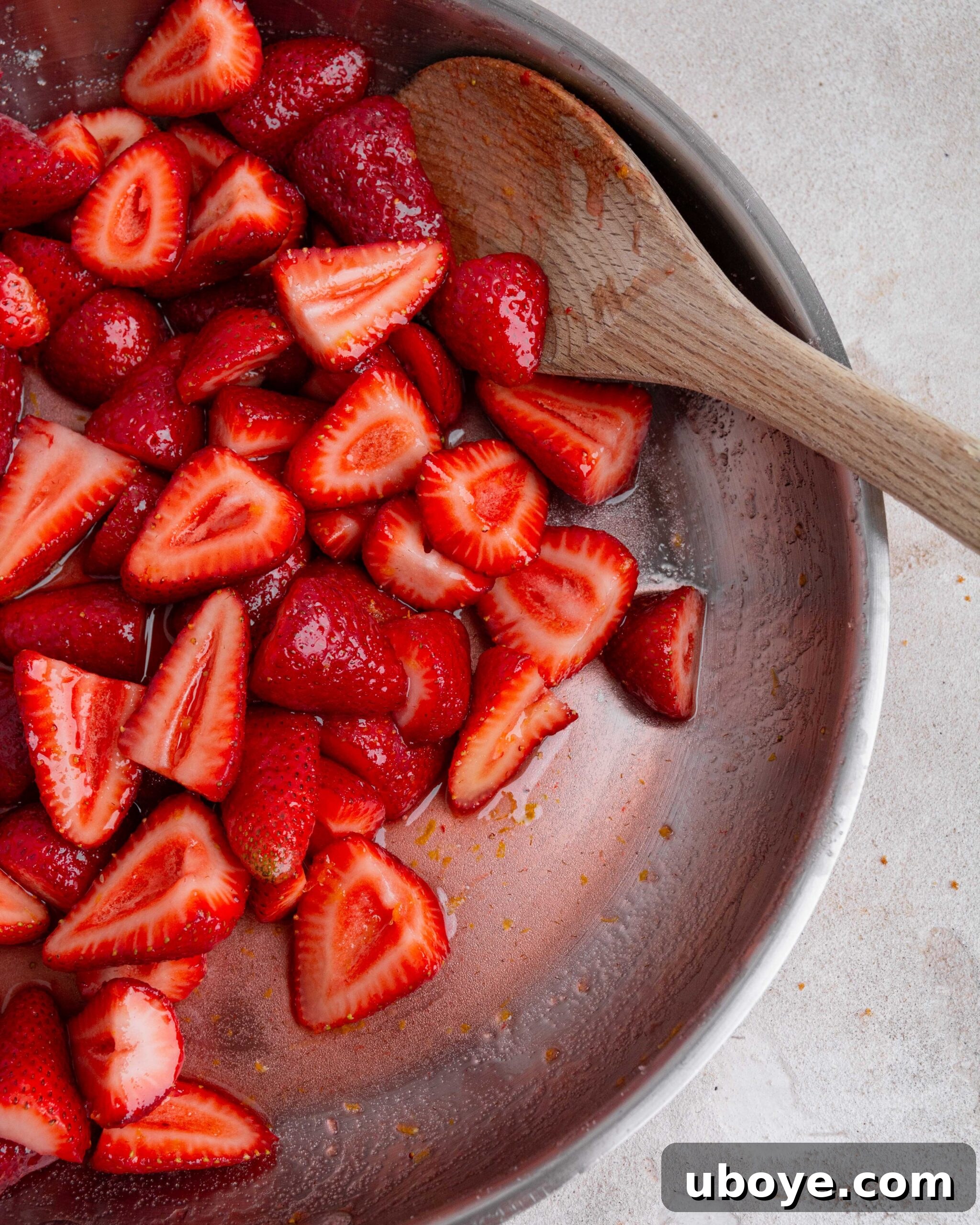 Sweet Focaccia with Strawberry Jam and Cream Cheese Glaze 4 Tossing the strawberries with sugar and lemon juice. Wooden spoon pokes out of pan.