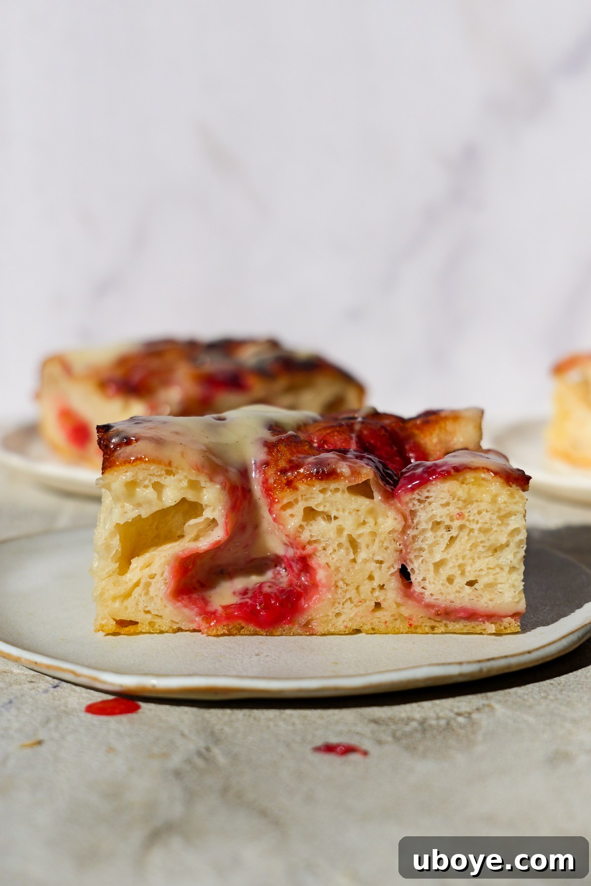 Sweet Focaccia with Strawberry Jam and Cream Cheese Glaze 10 A slice of strawberry jam focaccia sits on a white plate.