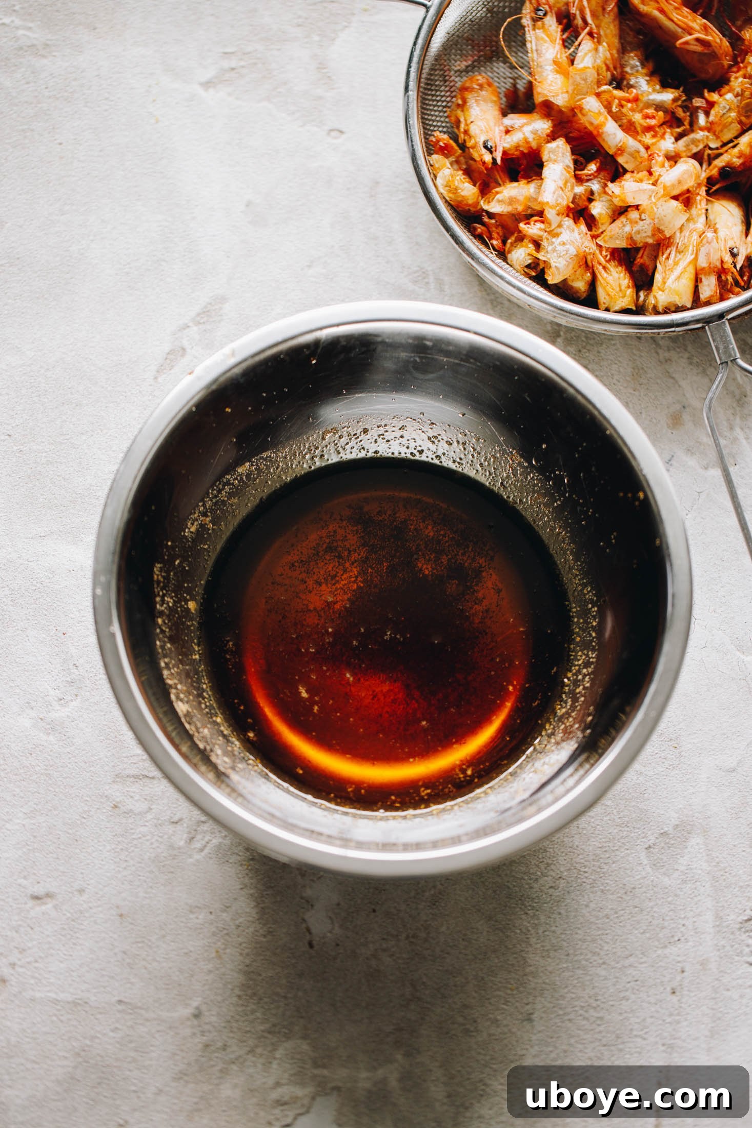 Rich orange-colored olive oil in a stainless steel bowl after straining prawn shells.