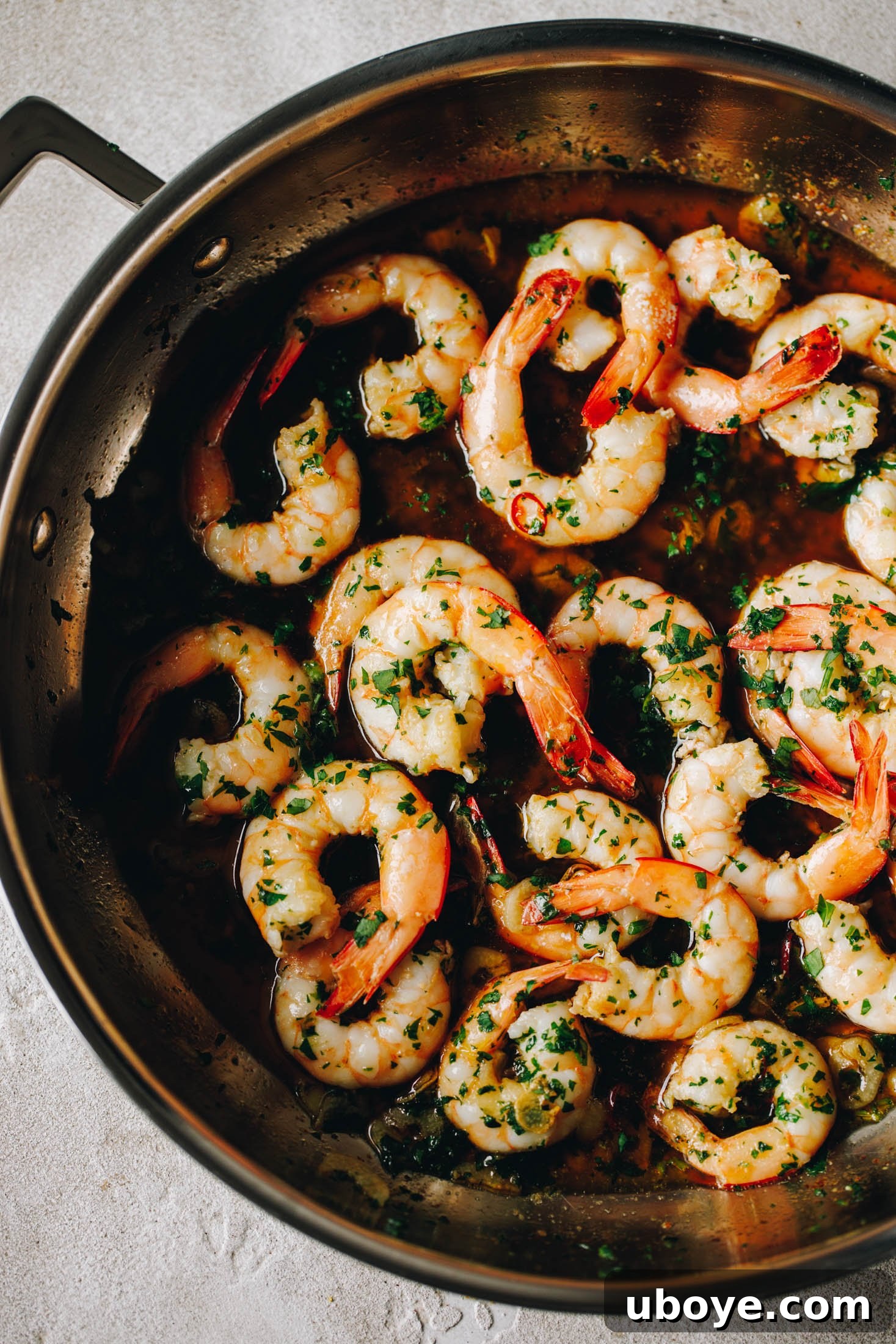 Peeled Spanish Garlic Shrimp (Gambas al Ajillo) sizzling in a large stainless steel fry pan with garlic and chili.