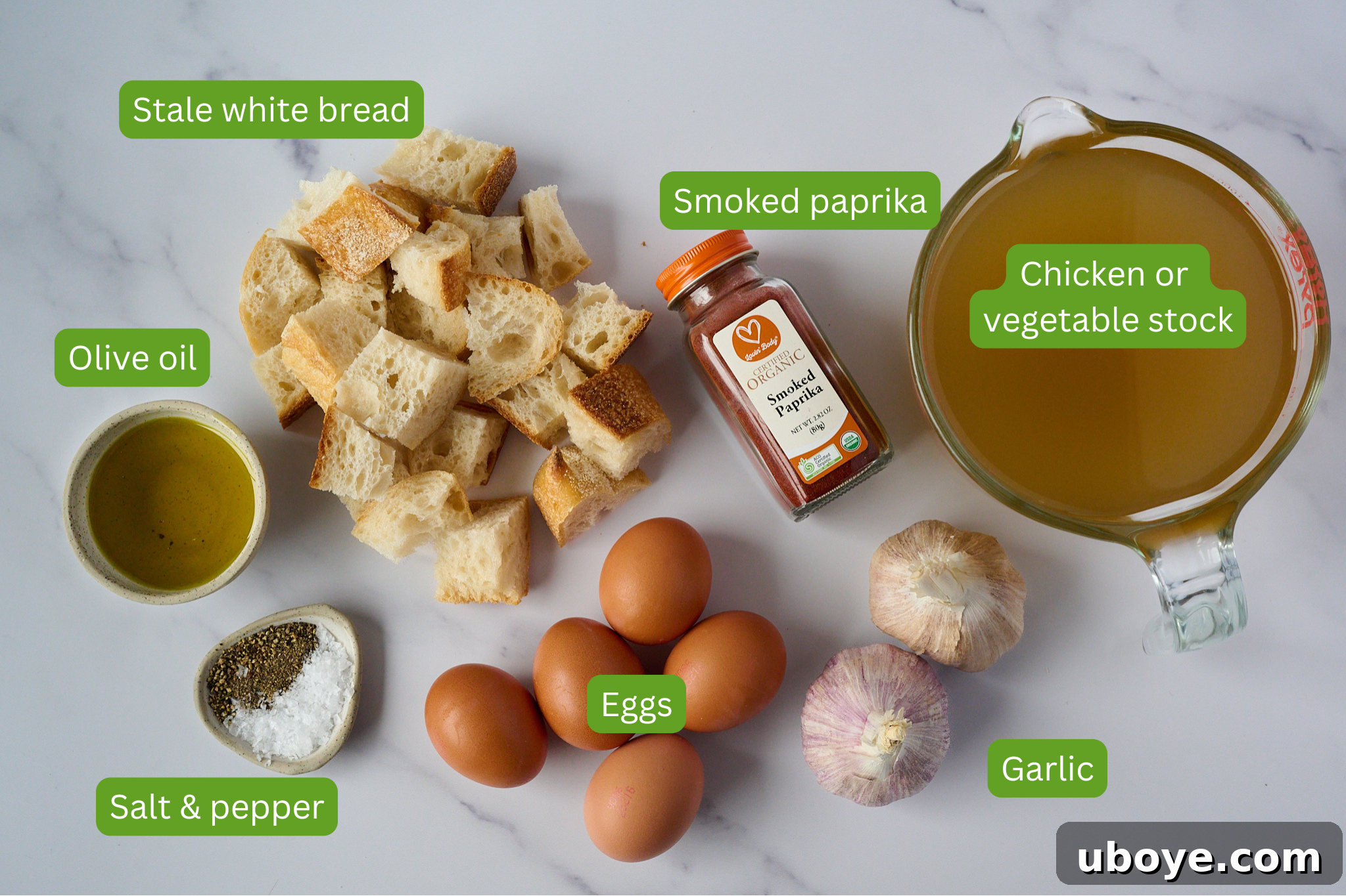 A vibrant flat lay of all the fresh and simple ingredients needed for Sopa de Ajo: garlic cloves, olive oil, smoked paprika, stale bread, broth, and eggs.