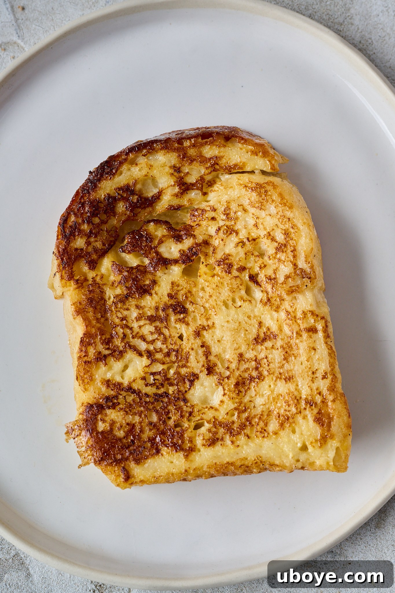 Torrijas Spain's Beloved French Toast 7 A perfectly fried, thick slice of white bread, golden and crispy, rests on a white plate, showcasing its irresistible Spanish crust.