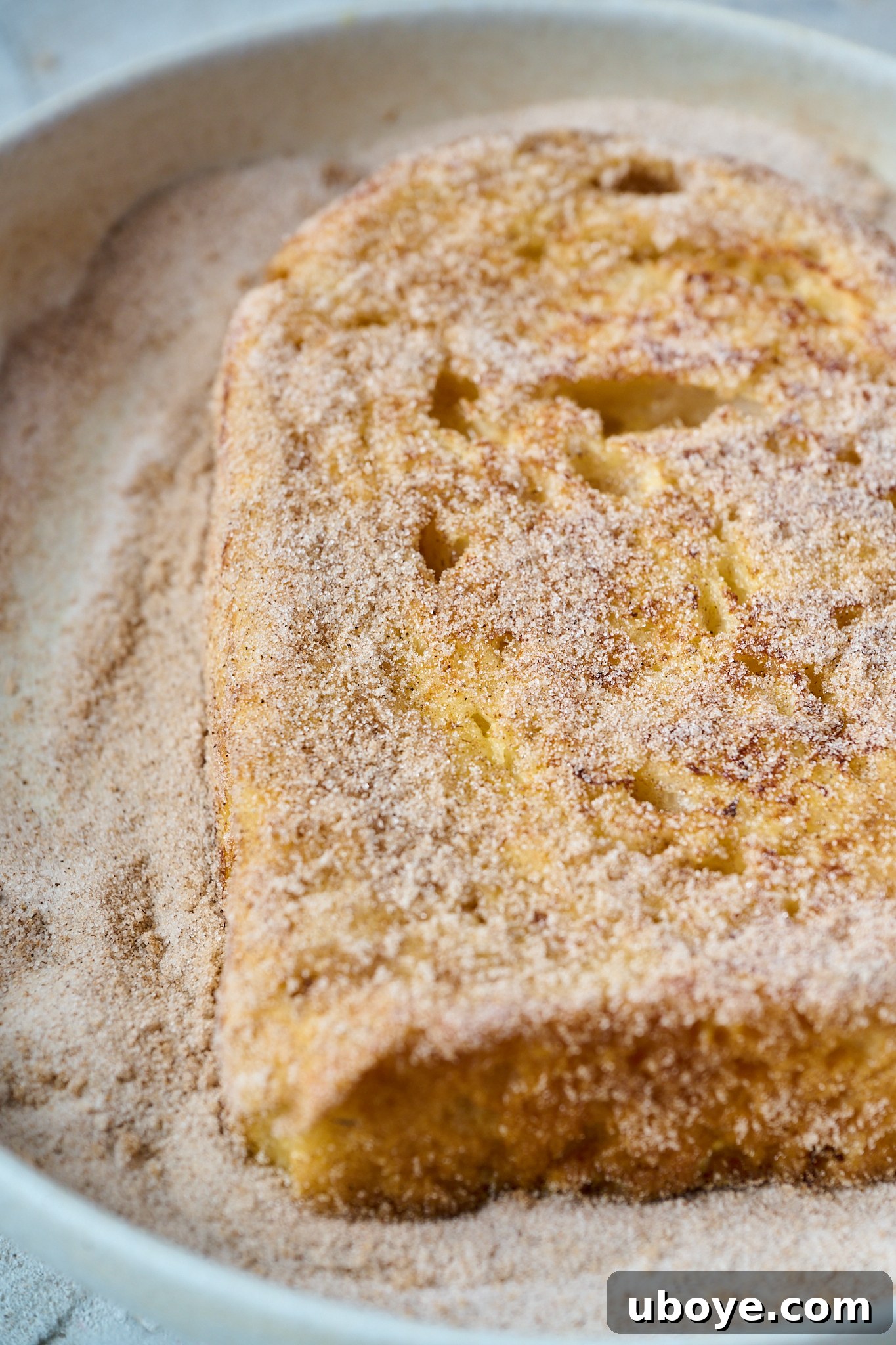 Torrijas Spain's Beloved French Toast 8 A freshly fried piece of Torrijas is being generously dusted with a mixture of cinnamon sugar, creating a delicious and aromatic coating.