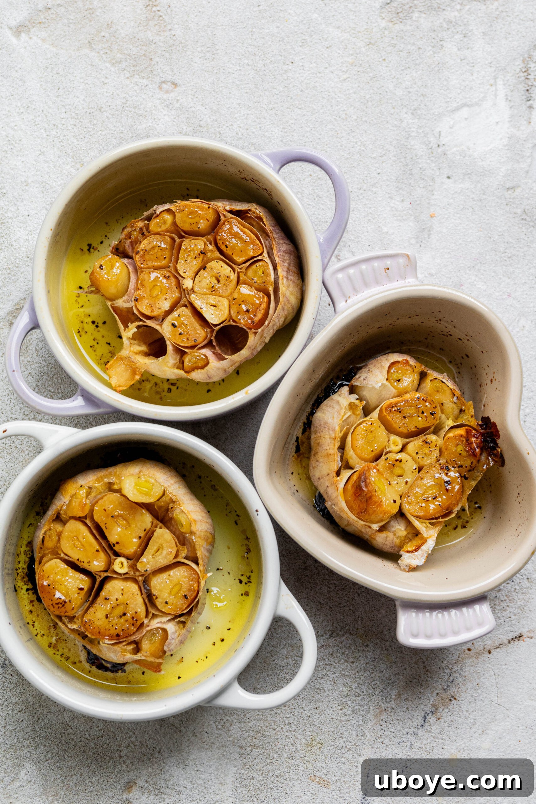 Three small pots filled with roasted garlic bulbs, showcasing the golden, tender appearance of garlic confit.