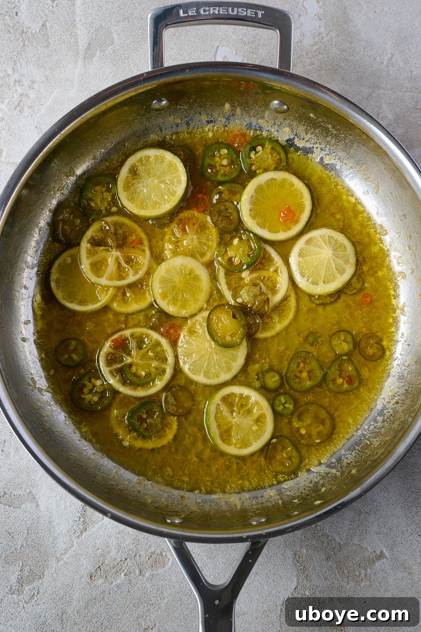 Honey-Chili Slow Roasted Salmon 7 Slightly caramelized limes and jalapeño slices are coated in a rich, buttery sauce within a large stainless steel frypan, indicating the next stage of sauce preparation.