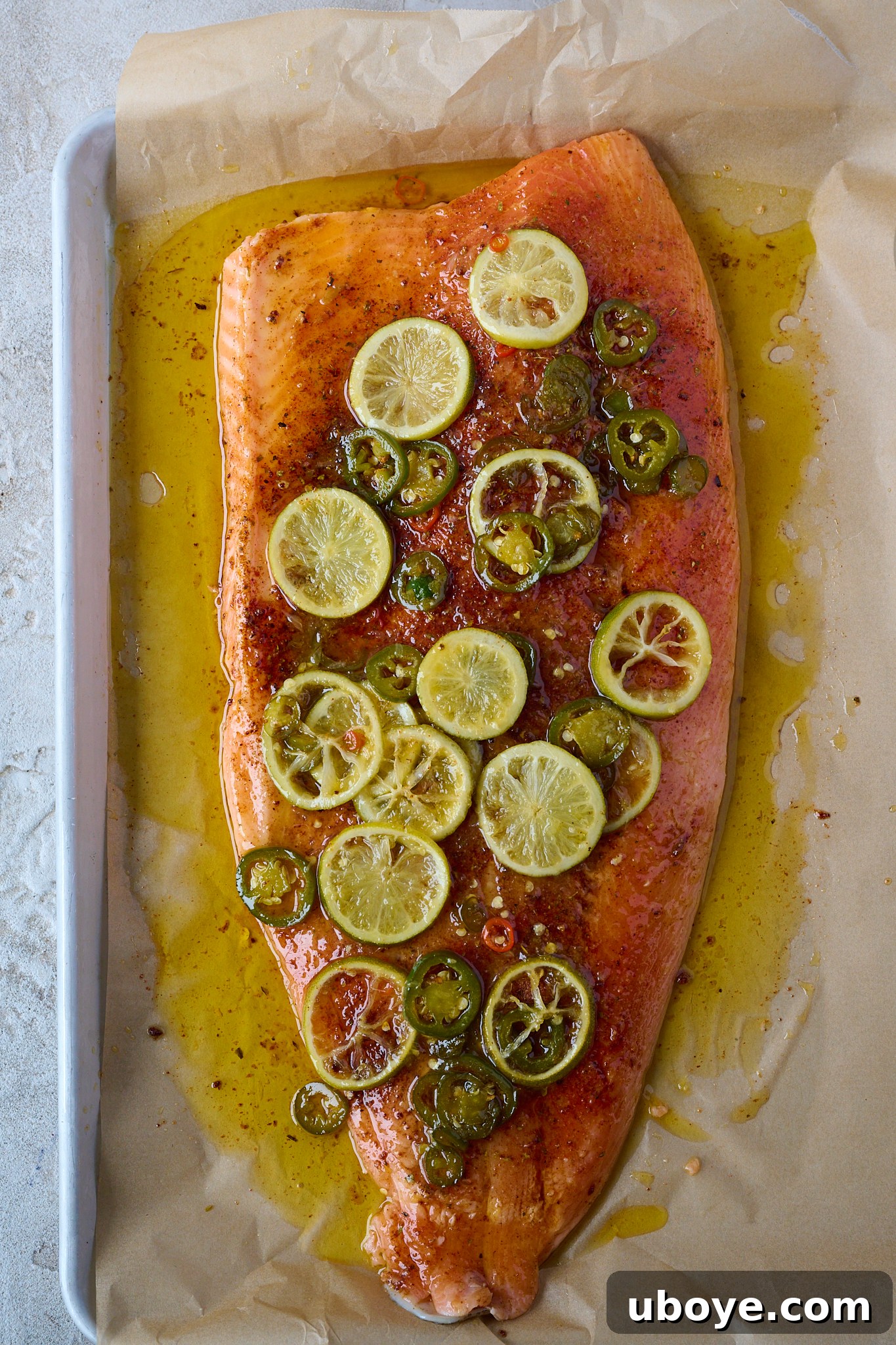 Honey-Chili Slow Roasted Salmon 8 A large salmon fillet, raw but coated in spices and now generously covered with the sticky hot honey sauce, complete with cooked lime slices and jalapeños, sits on a baking tray before being placed in the oven.