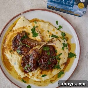 Three lamb chops resting on a pile of creamy mashed potatoes with sauce drizzled over.