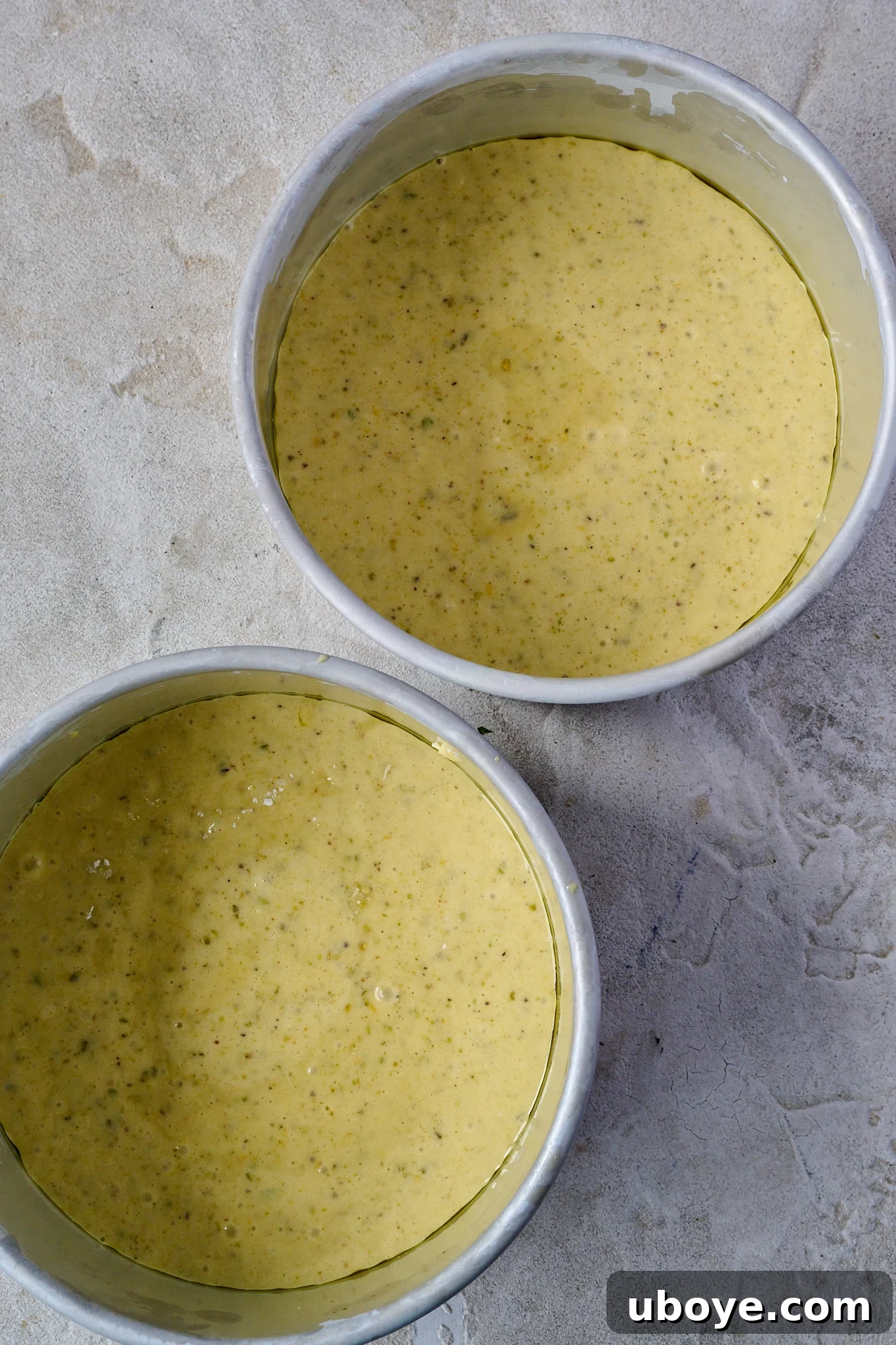 Velvet Olive Oil Cake with Pistachio, Raspberry and White Chocolate 6 Two round cake tins filled with the vibrant green batter of the White Chocolate, Pistachio & Raspberry Olive Oil Cake, ready for baking.
